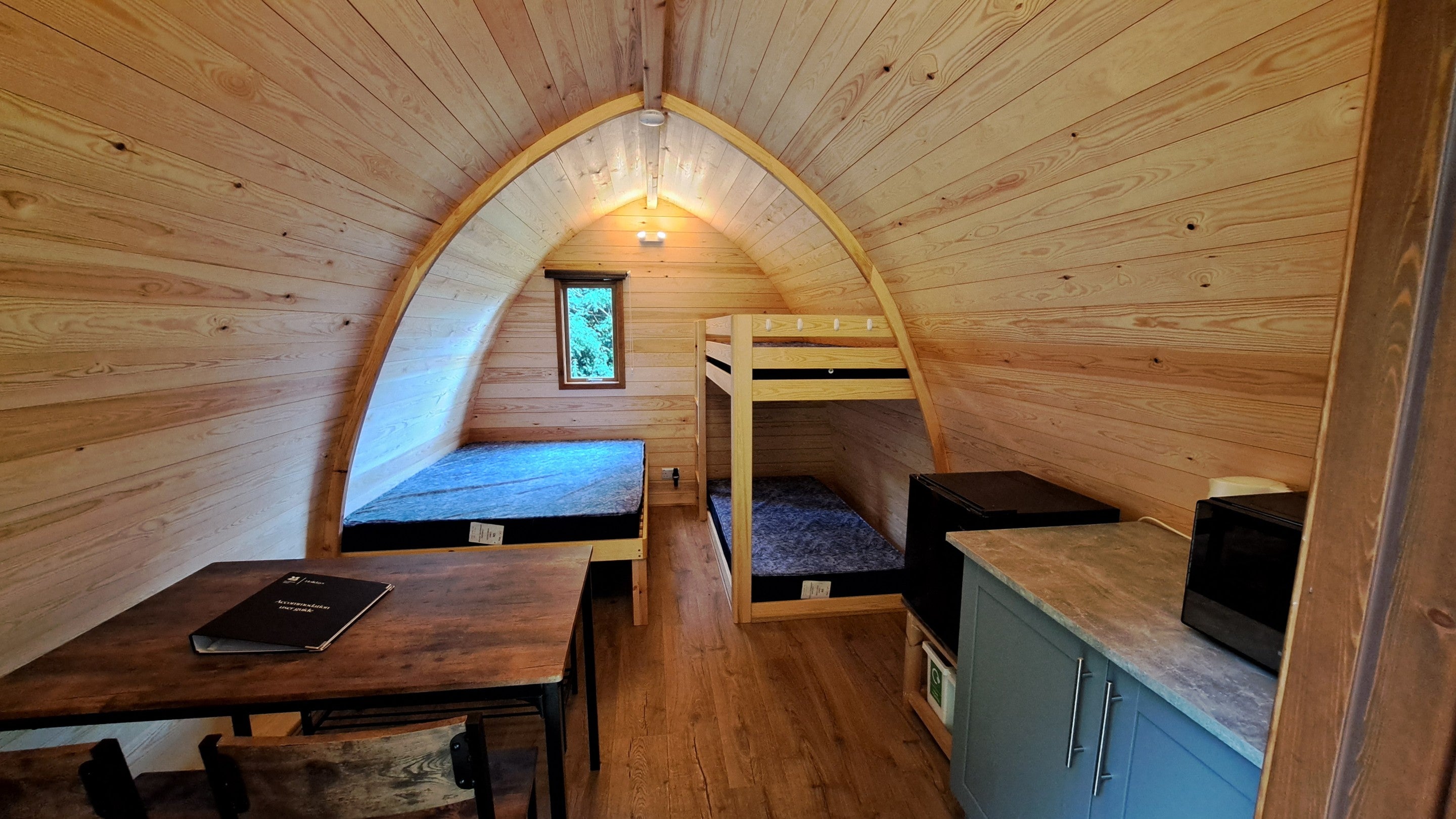 The interior of one of the Furnished Pods, with fixed double bed and bunkbed, table and chairs at Waterclose Meadows, Cambridgeshire