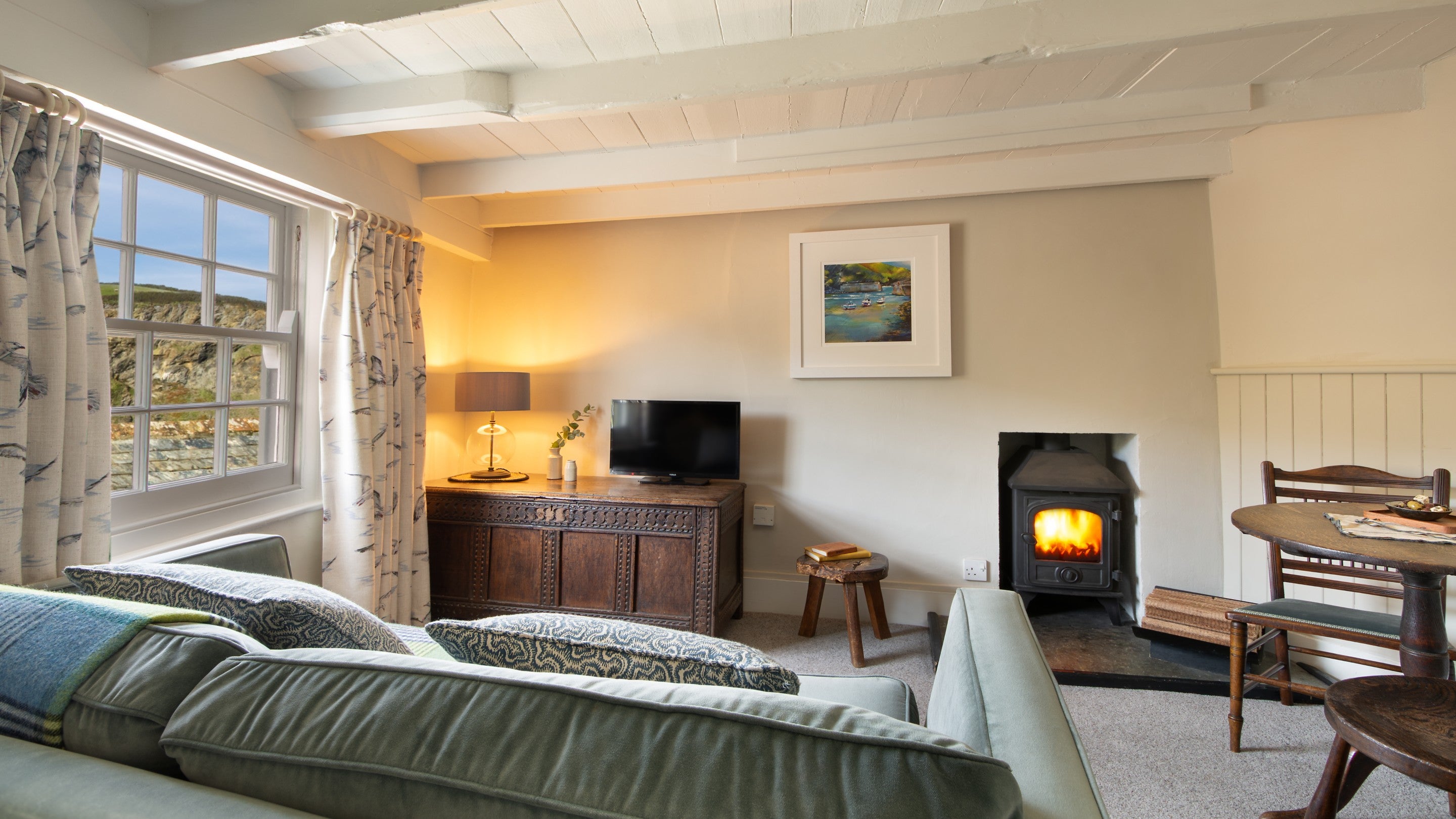 The sitting room on the first floor of The Birdcage, with sofa, television, woodburner and table for two, Cornwall