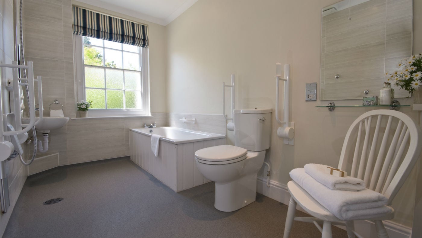 The bathroom at The Captain's Quarter, with grab rails, a folding seat under the shower, and a separate bath, Cornwall