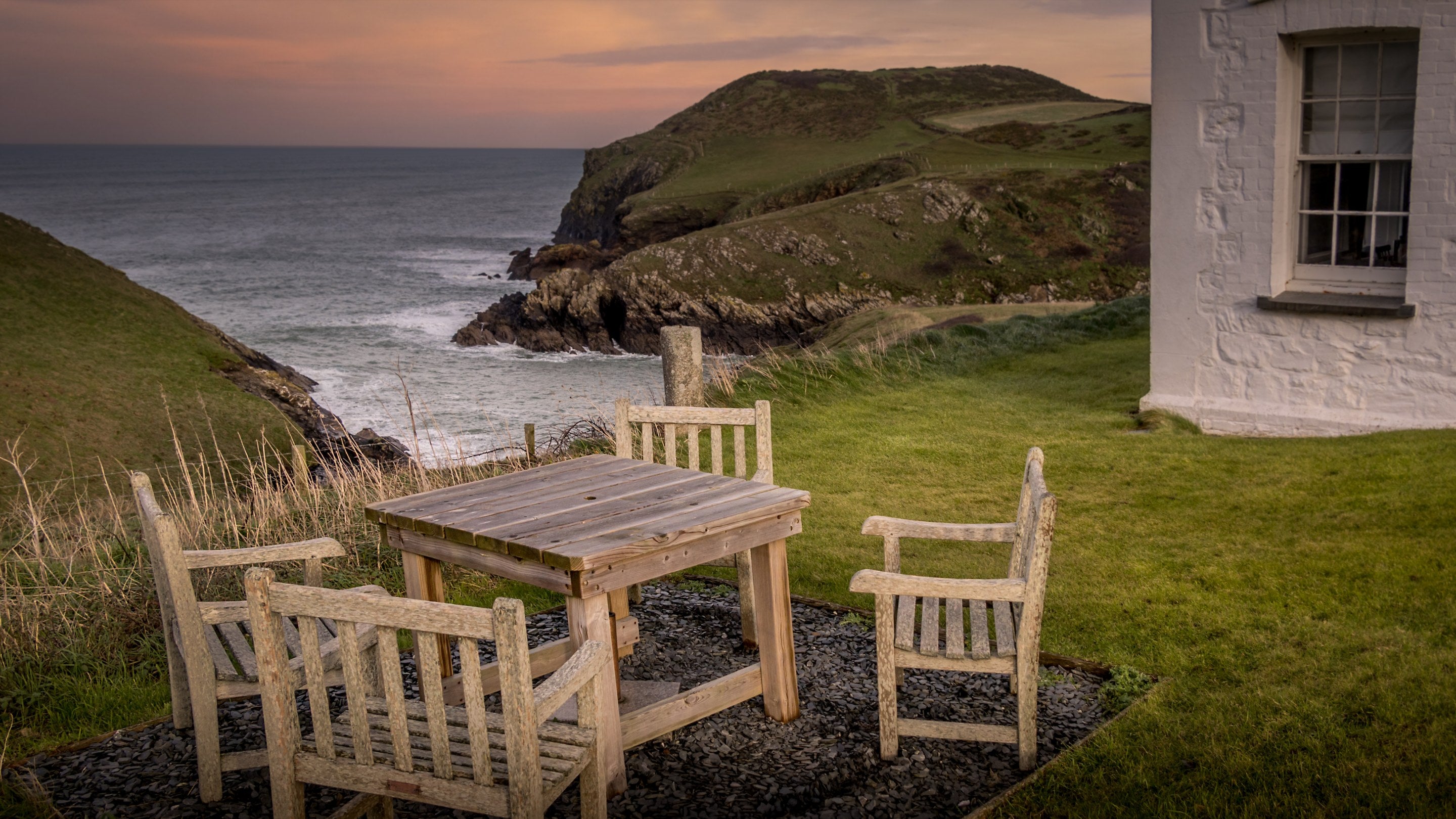 The shared garden with outdoor furniture at Carnweather, overlooking the cliffs and sea around Port Quin, Cornwall