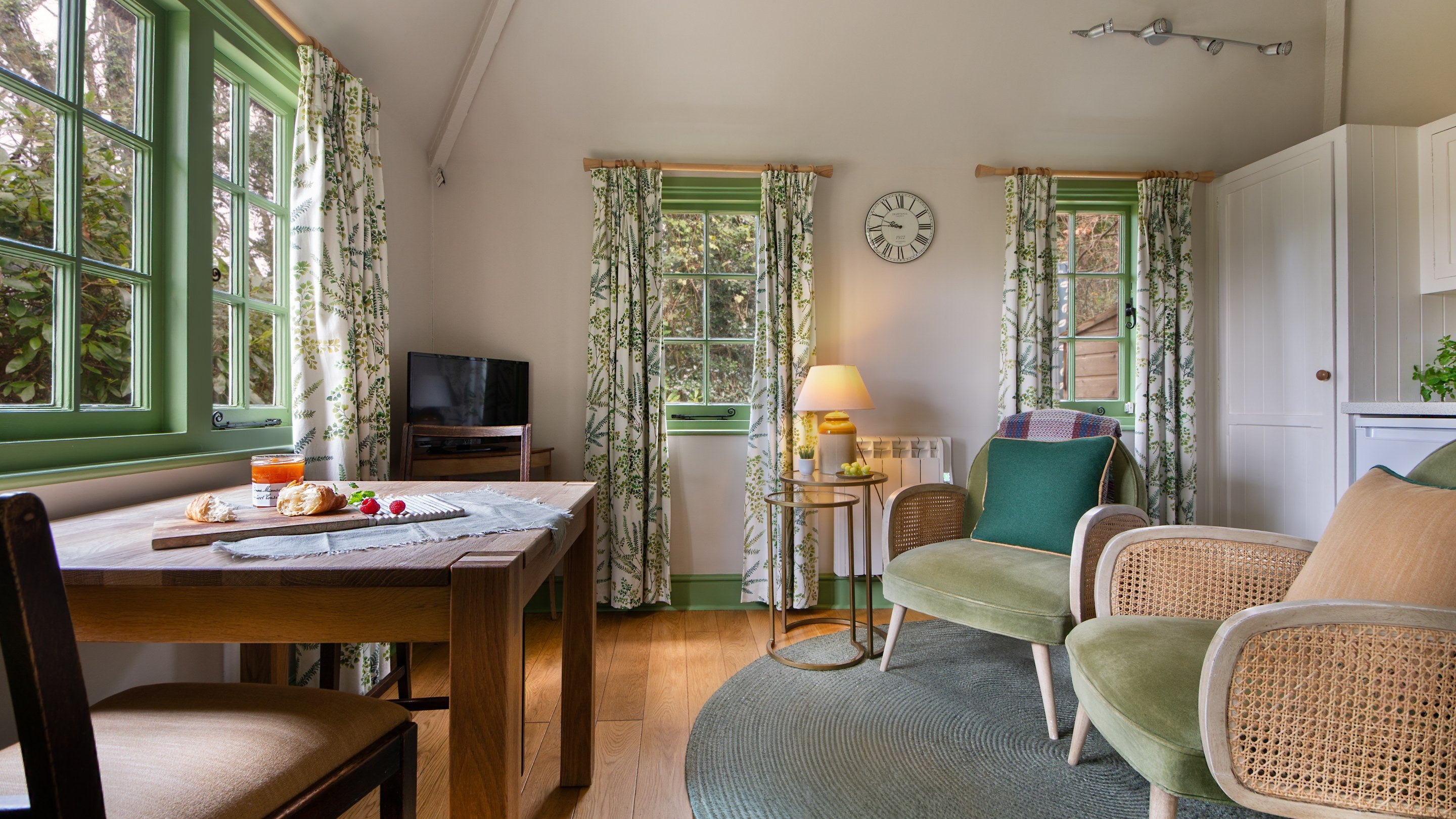 The sitting and dining area of the open-plan living space at Durgan Wood Cottage, with table for two, small television and two armchairs, Cornwall