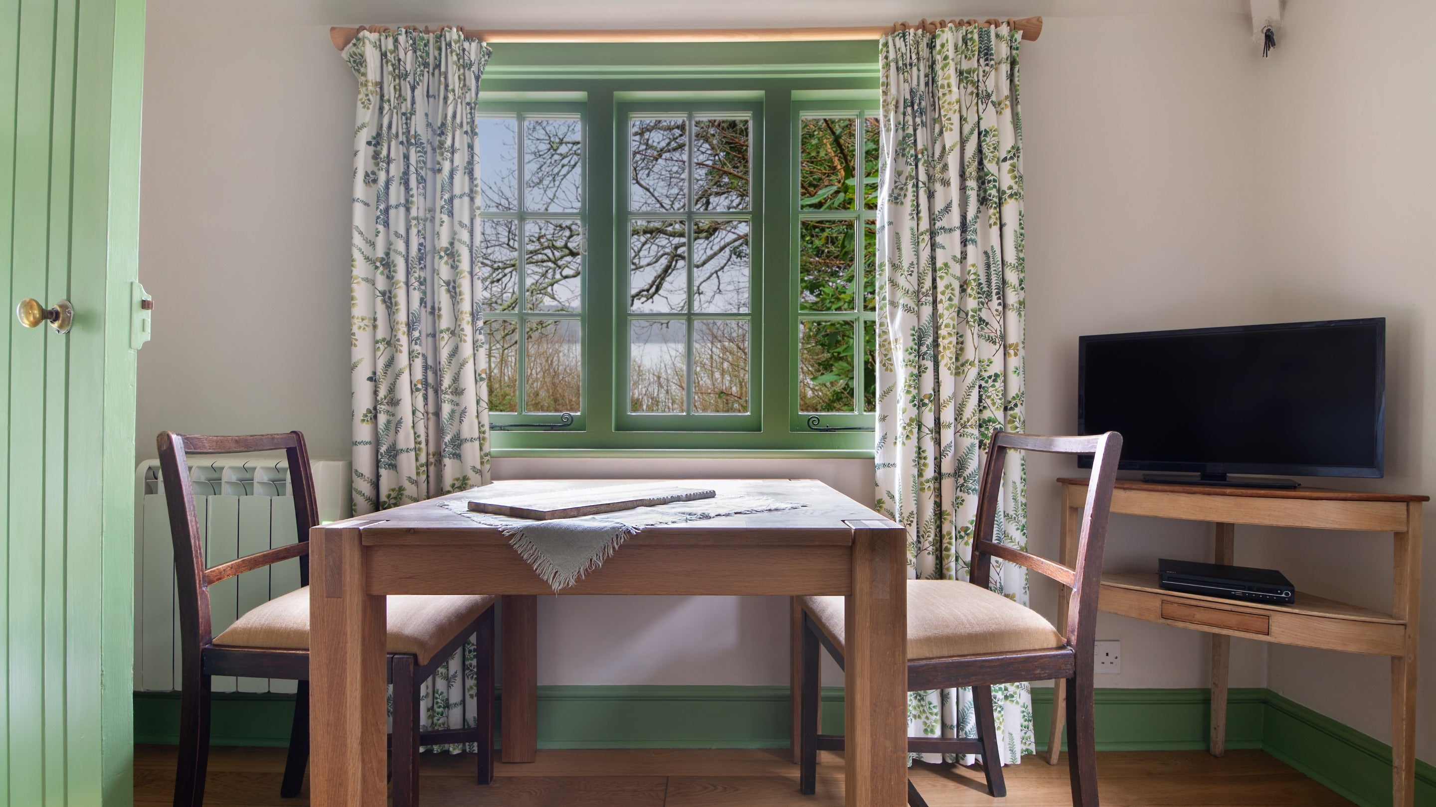 The large window above the table in the living space at Durgan Wood Cottage with views toward the Helford River, Cornwall