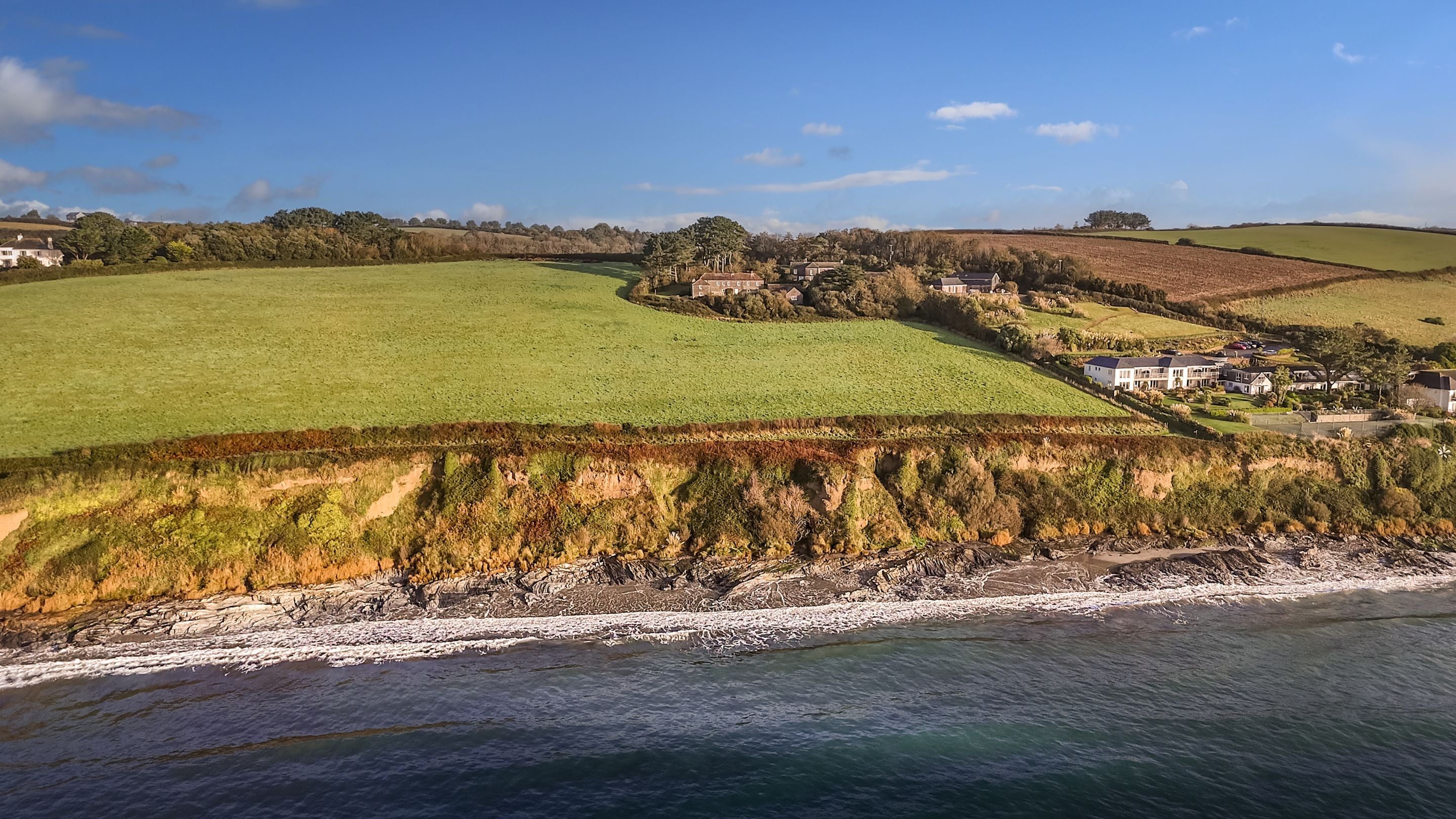 An aerial view of the Gwendra cottages on the cliff above Pendower beach at high tide, Cornwall