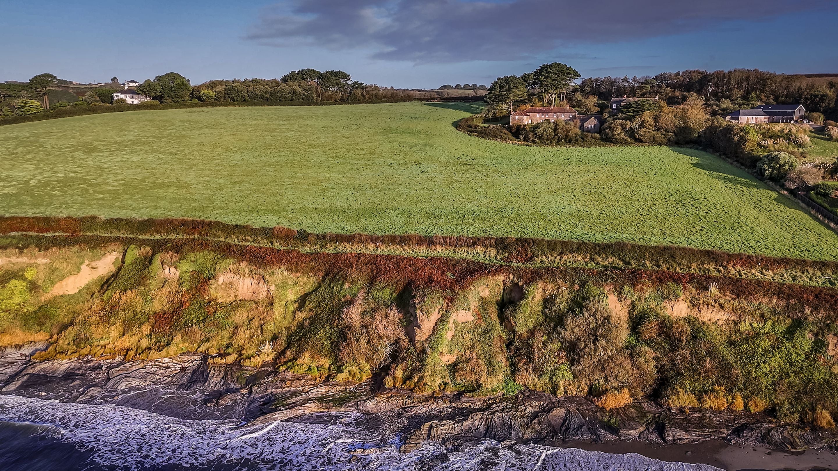 An aerial view of the Gwendra cottages on the cliff above Pendower beach at high tide, Cornwall