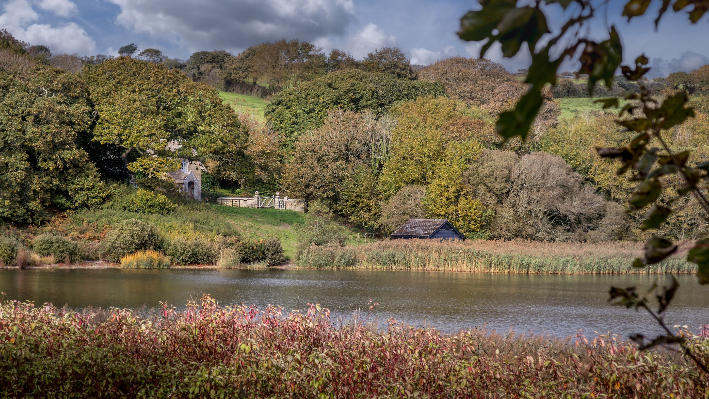 Helston Lodge, partially hidden by trees and viewed from across Loe Pool, Cornwall