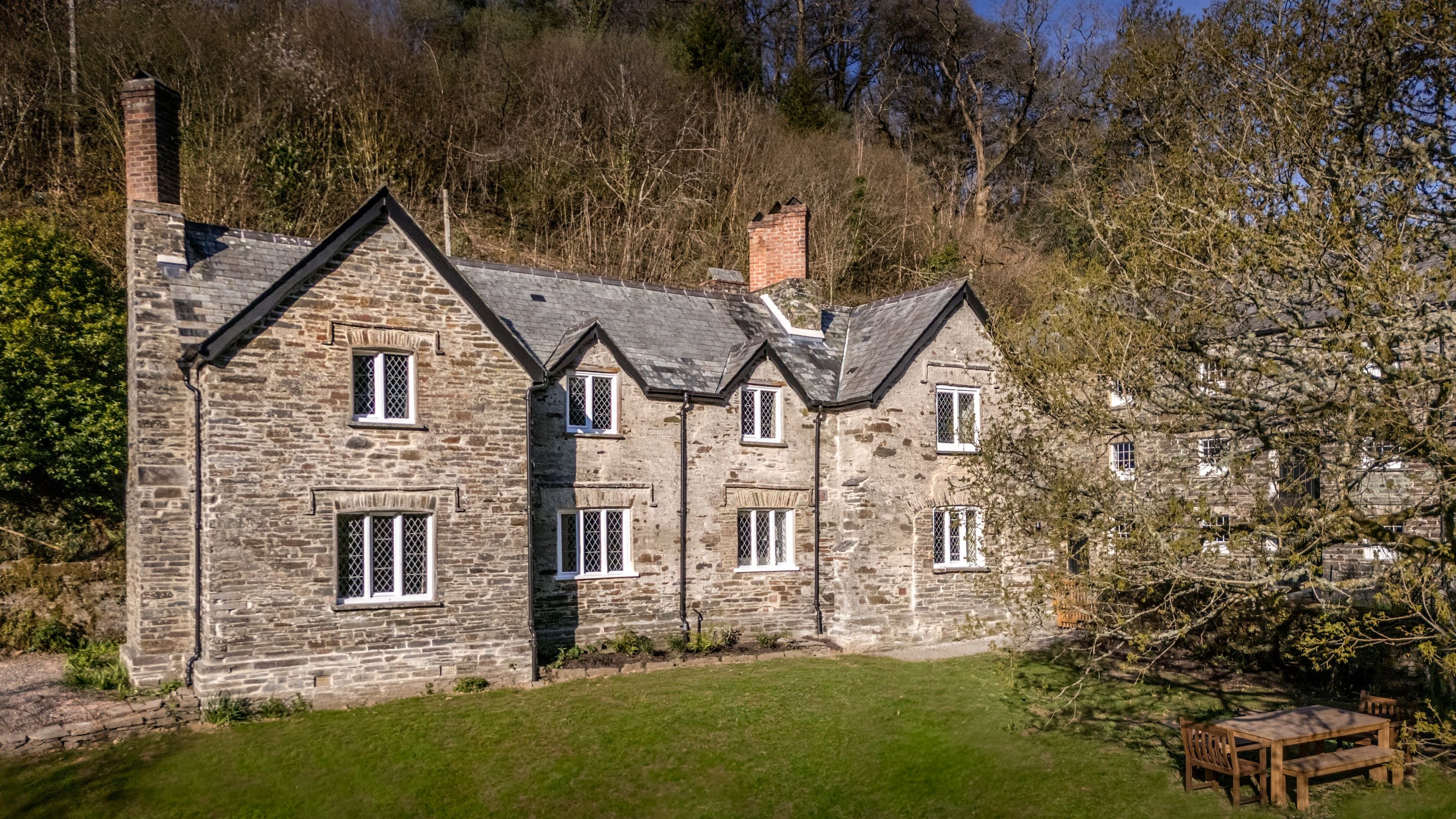The back of Miller's House and its garden, with lawn, outdoor dining furniture and trees, Cornwall