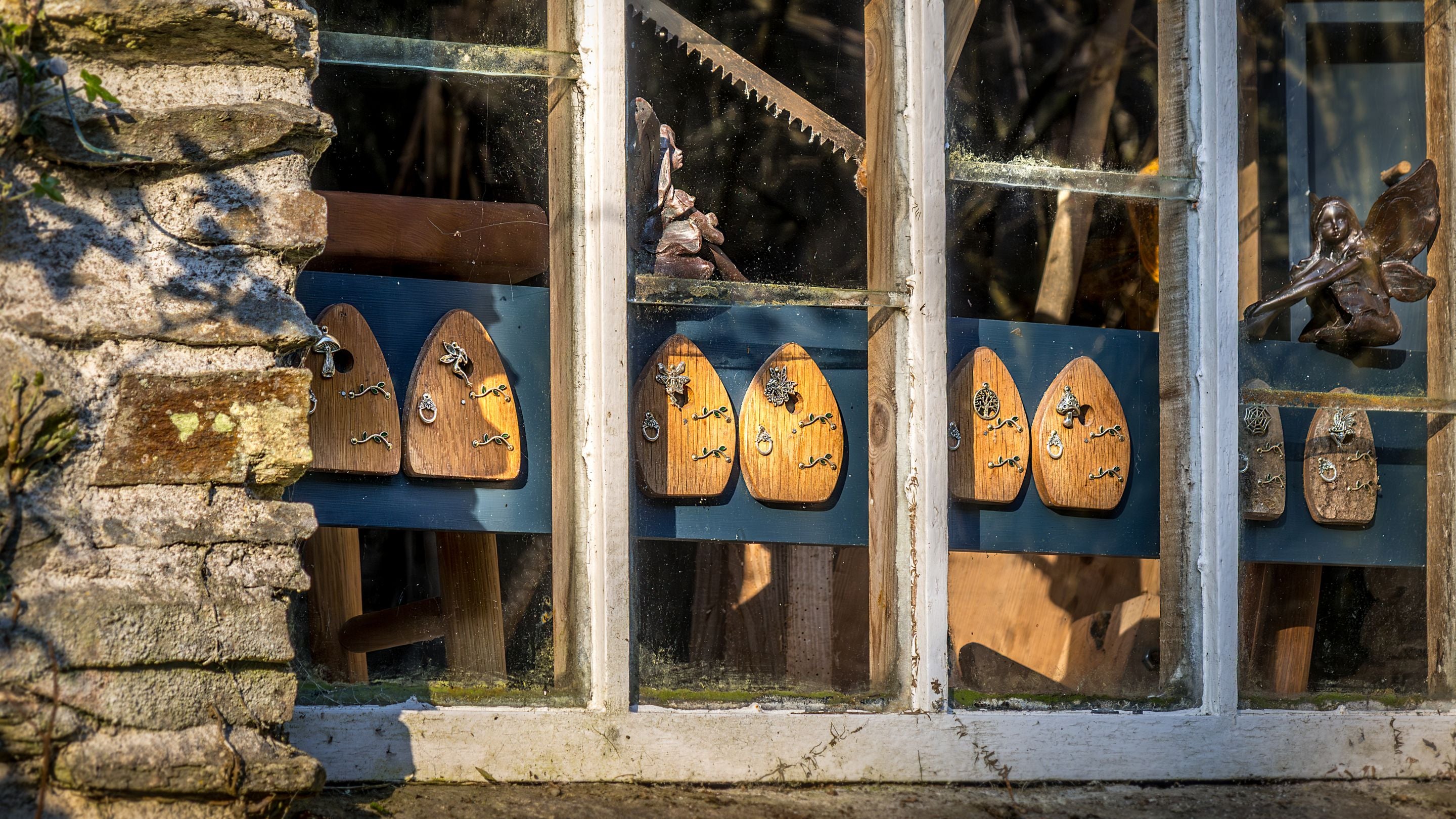 The window of one of the craft workshops near Miller's House, with small fairy doors and statues, Cornwall