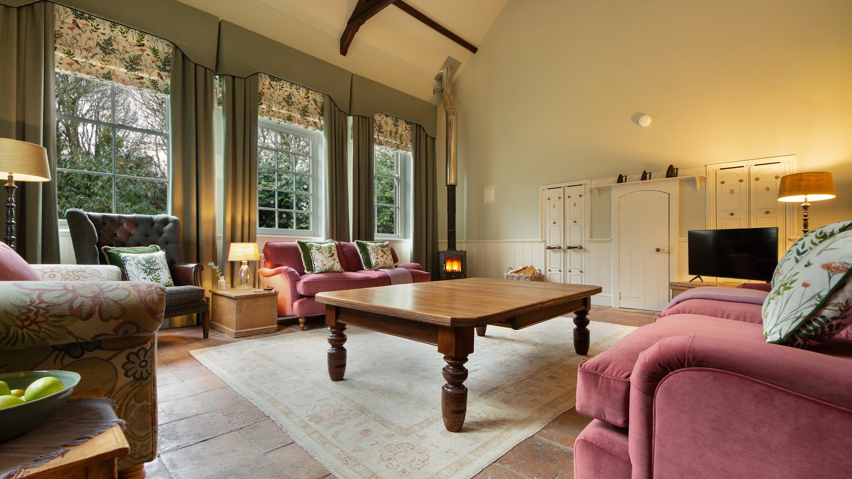 The sitting room at Nanceglos House, with a vaulted ceiling, four large windows, three sofas, an armchair, a woodburner and a television, Cornwall