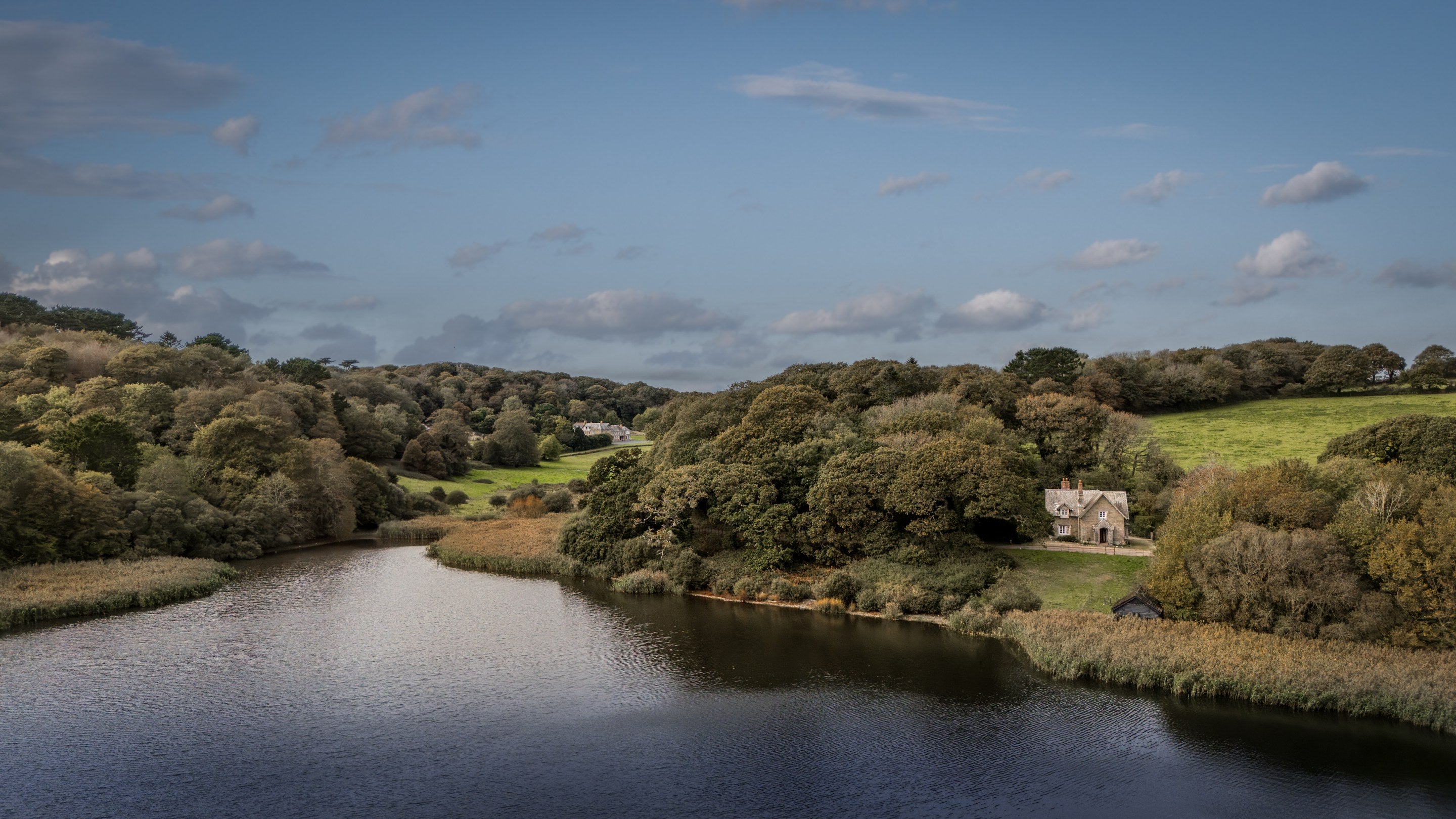 An aerial view of Loe Pool lake, surrounded by woods and parkland at Penrose, Cornwall