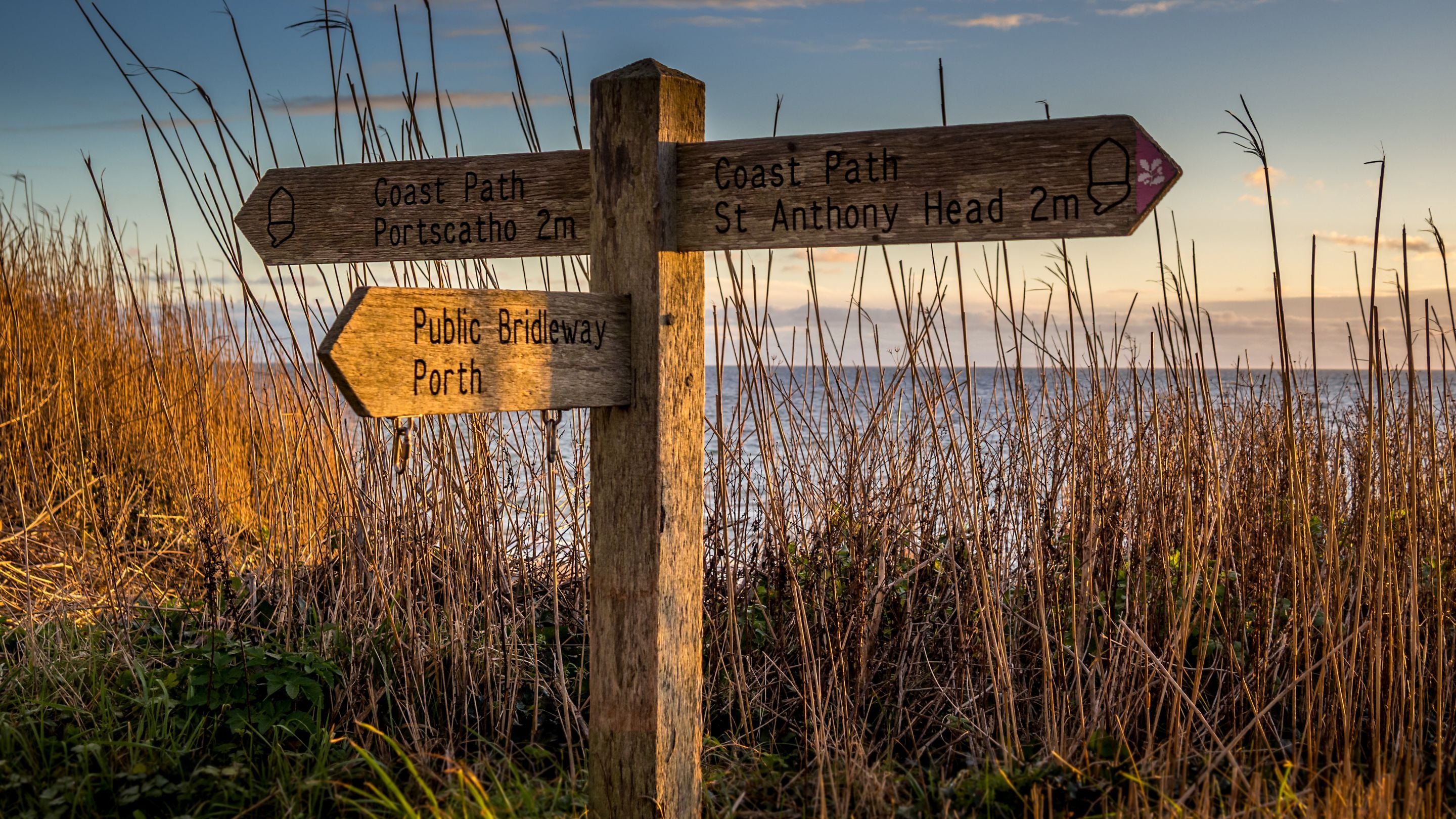 Coastal footpath sign near Roseland Porth Barn, showing the two-mile routes to St Anthony Head and Portscatho, Cornwall
