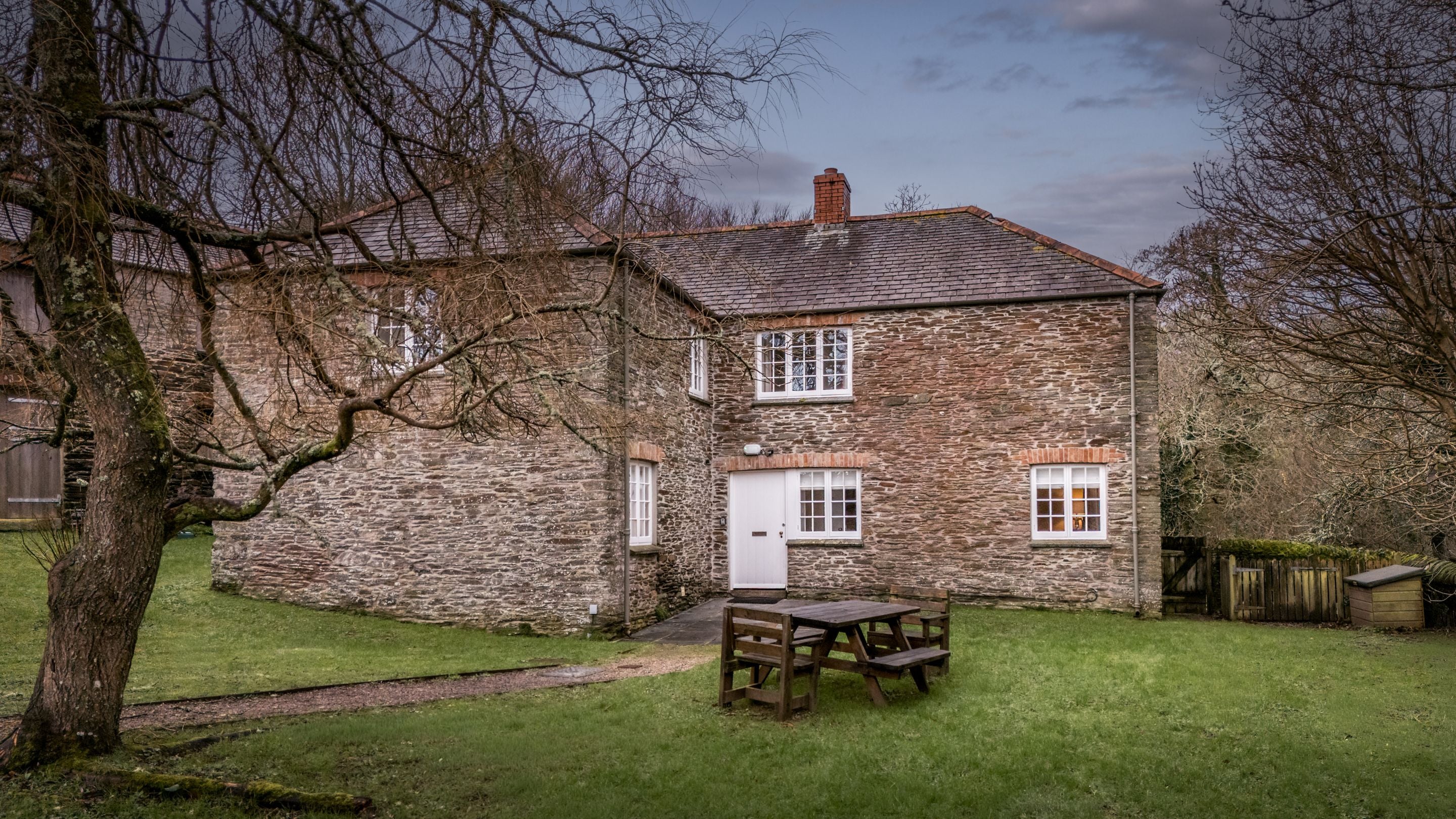 The exterior of Roseland Porth Barn and its lawned garden with outdoor dining furniture, Cornwall