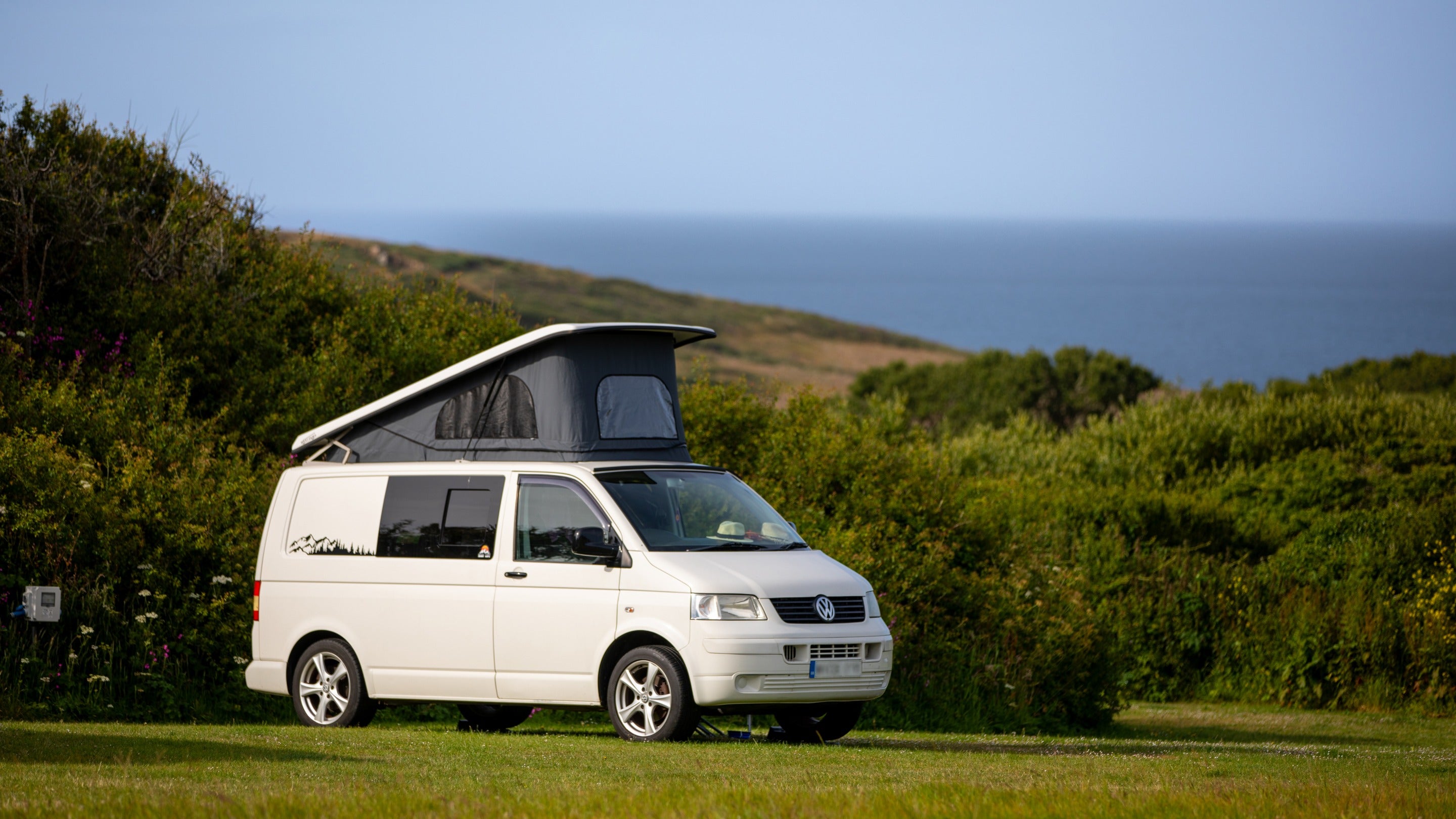 A campervan at Teneriffe Farm Campsite with the sea in the background, Cornwall