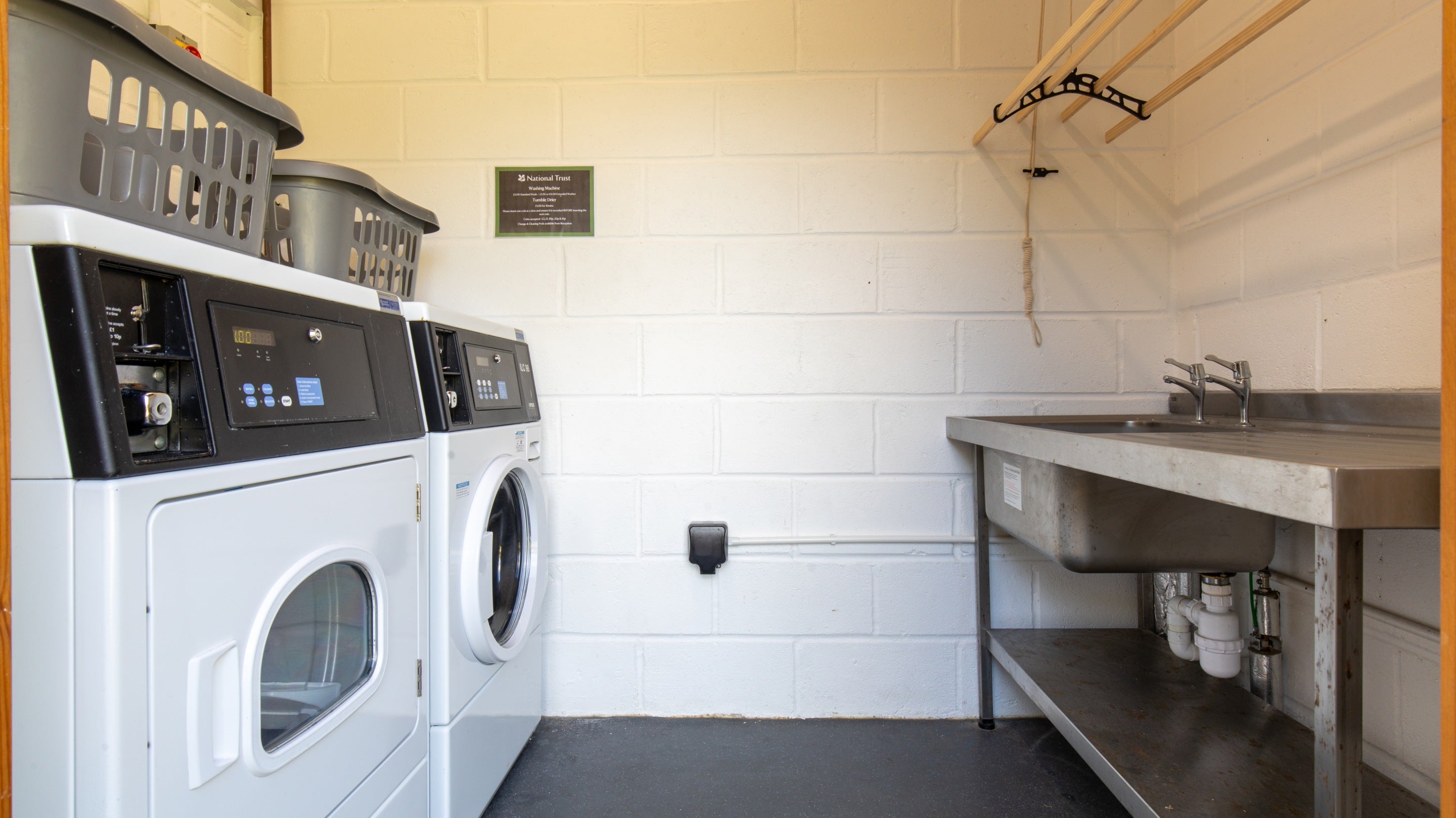 The laundry facility with coin-operated washing and drying machines and a sink for handwashing at Teneriffe Farm Campsite, Cornwall