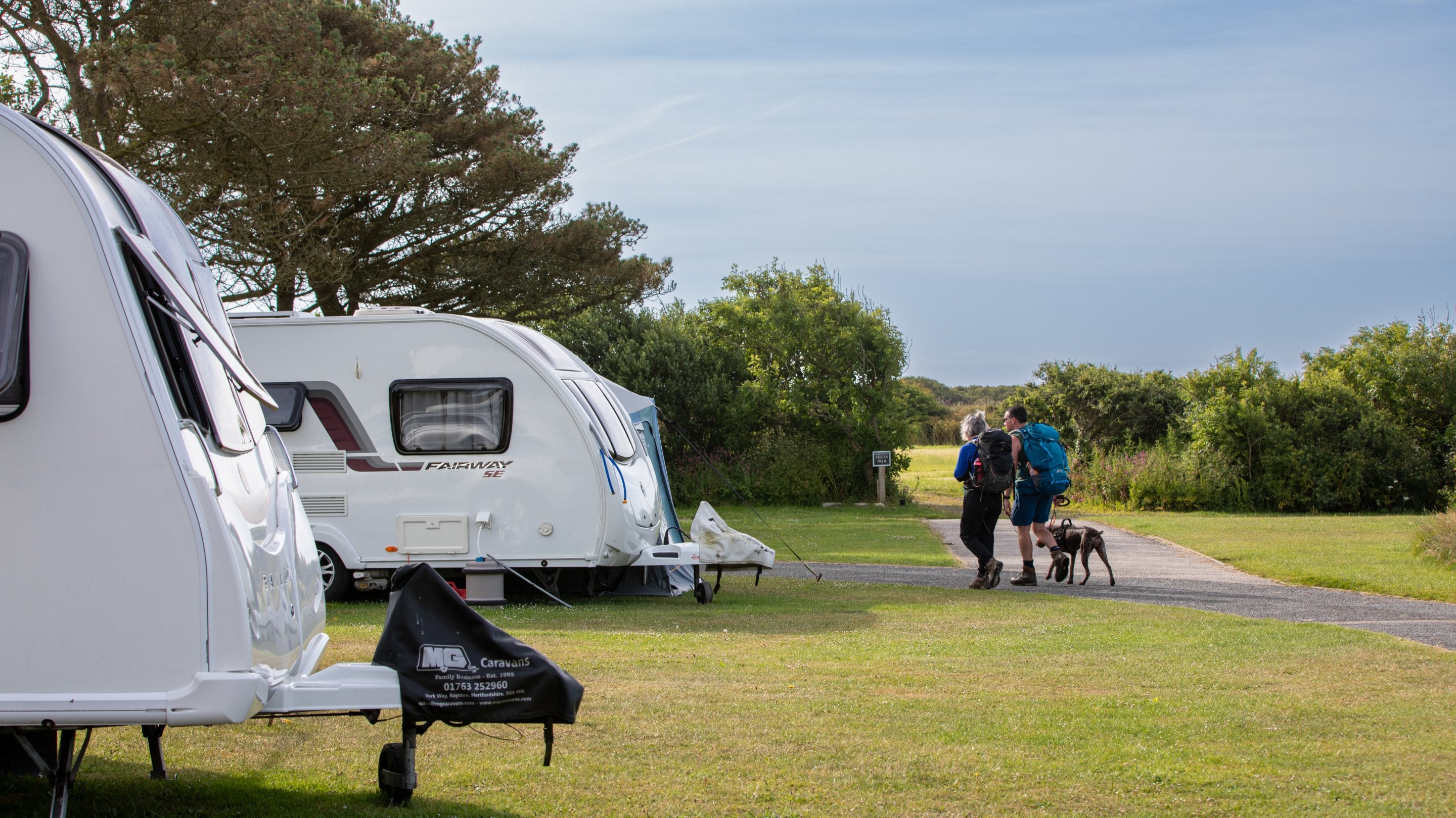 Guests walking past caravans with their dog, heading out for a walk from Teneriffe Farm Campsite, Cornwall