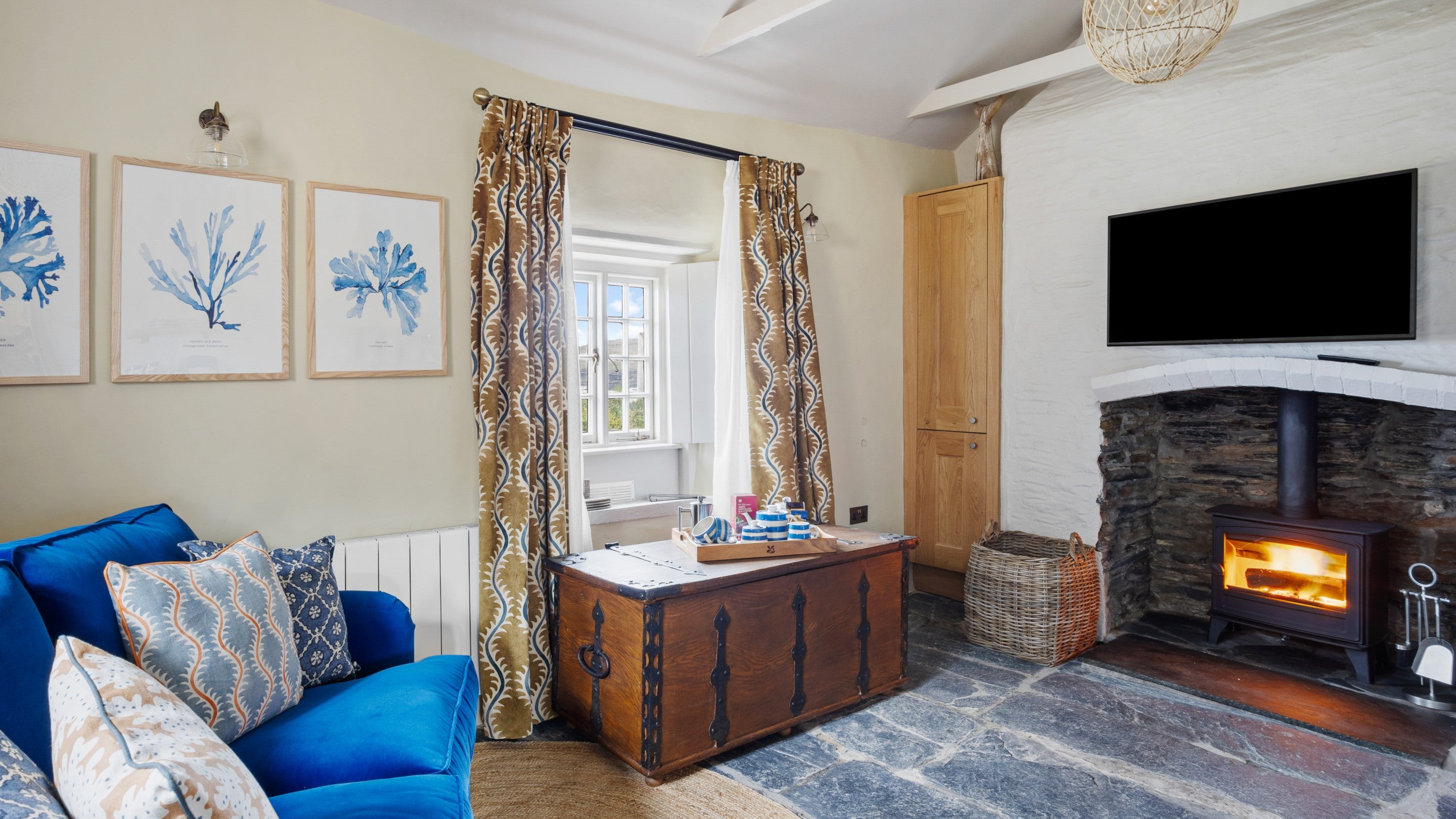 A view of the living space at Tom Parsons' Hut, showing the sofa, woodburner and window with sea views, Cornwall