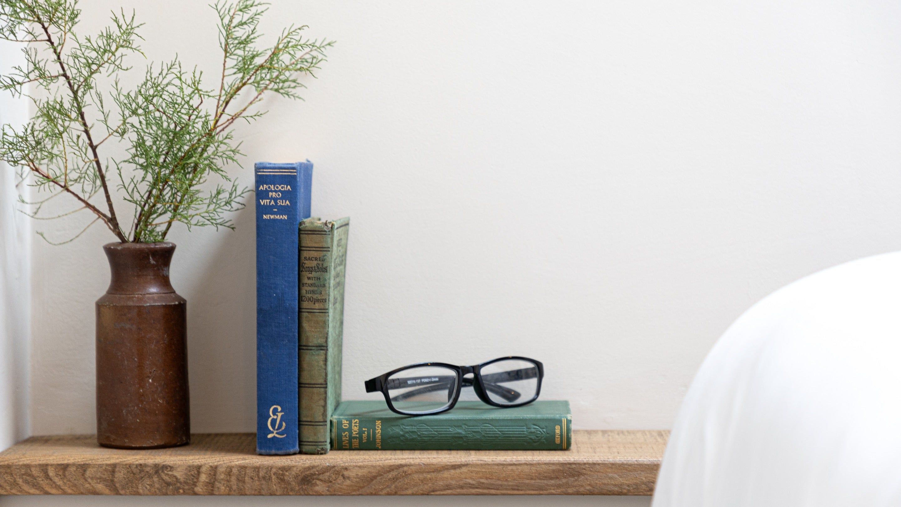 A pair of reading glasses and books on the wooden shelf near the bed at Tom Parsons' Hut, Cornwall