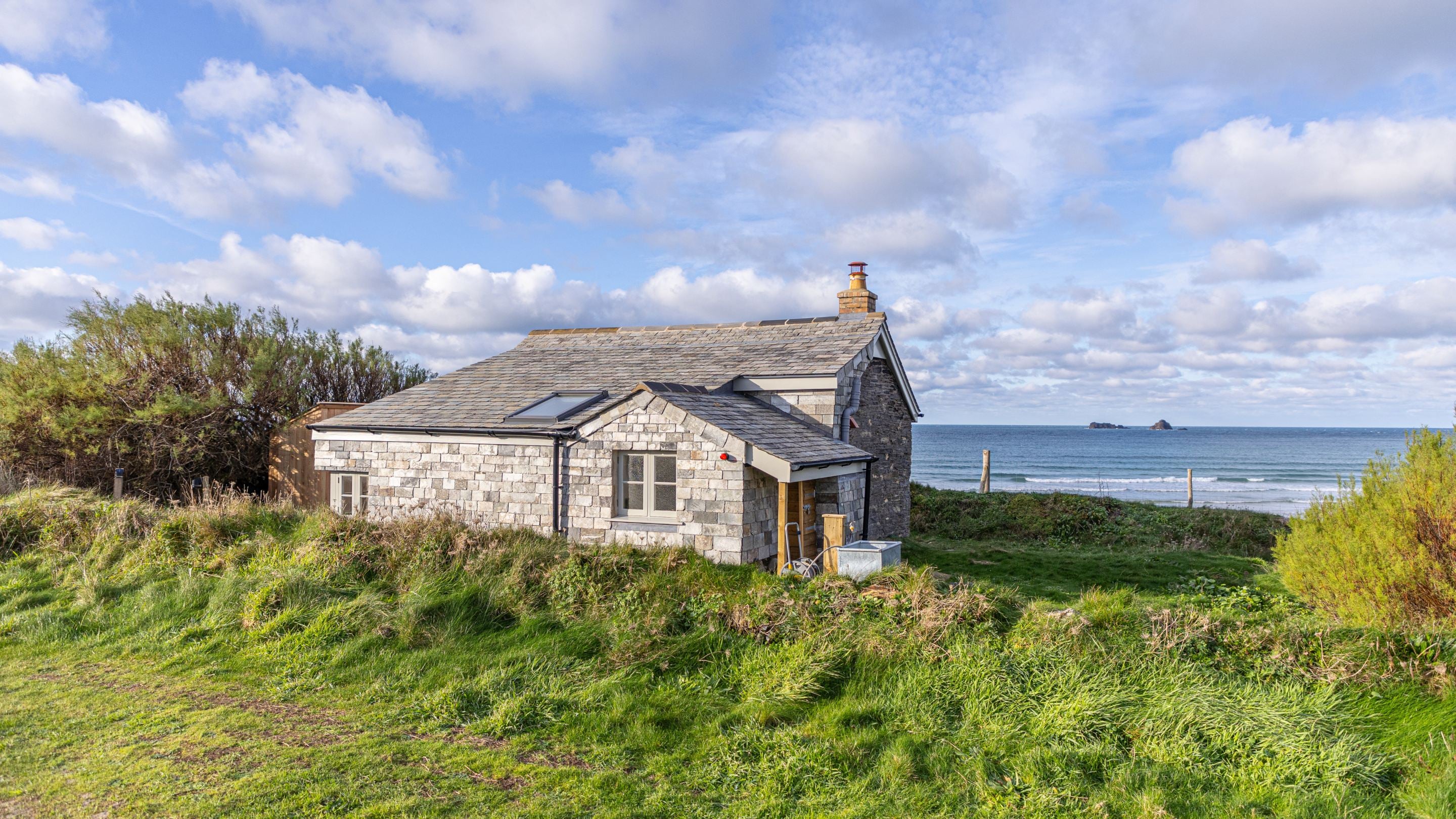 The exterior of Tom Parsons' Hut, viewed from the parking space with the sea in the distance, Cornwall