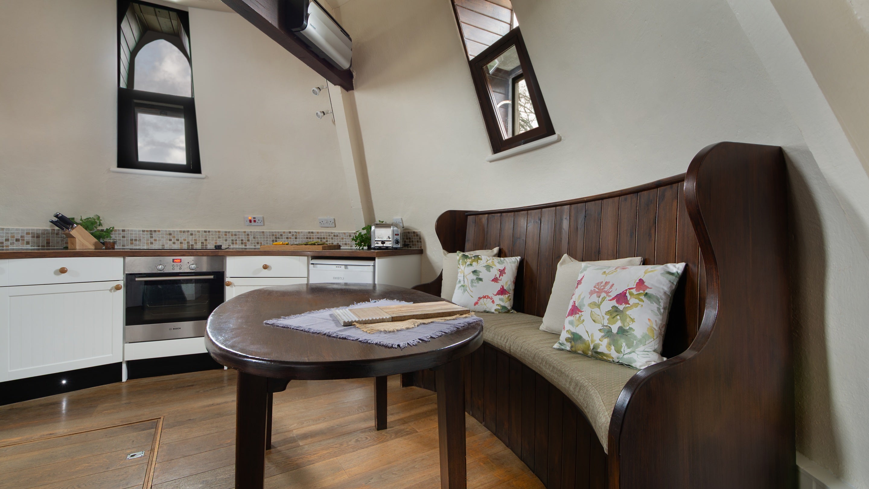 The kitchen-diner, a circular room on the top floor of Trelissick Water Tower, with curved bench seating by the dining table, Cornwall