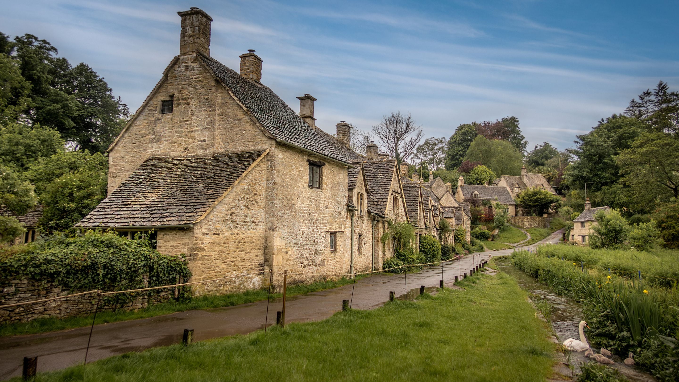 Arlington Row and the water meadow, with a swan and signets in the water. Number 1 is at the end of the terrace on the left, Gloucestershire
