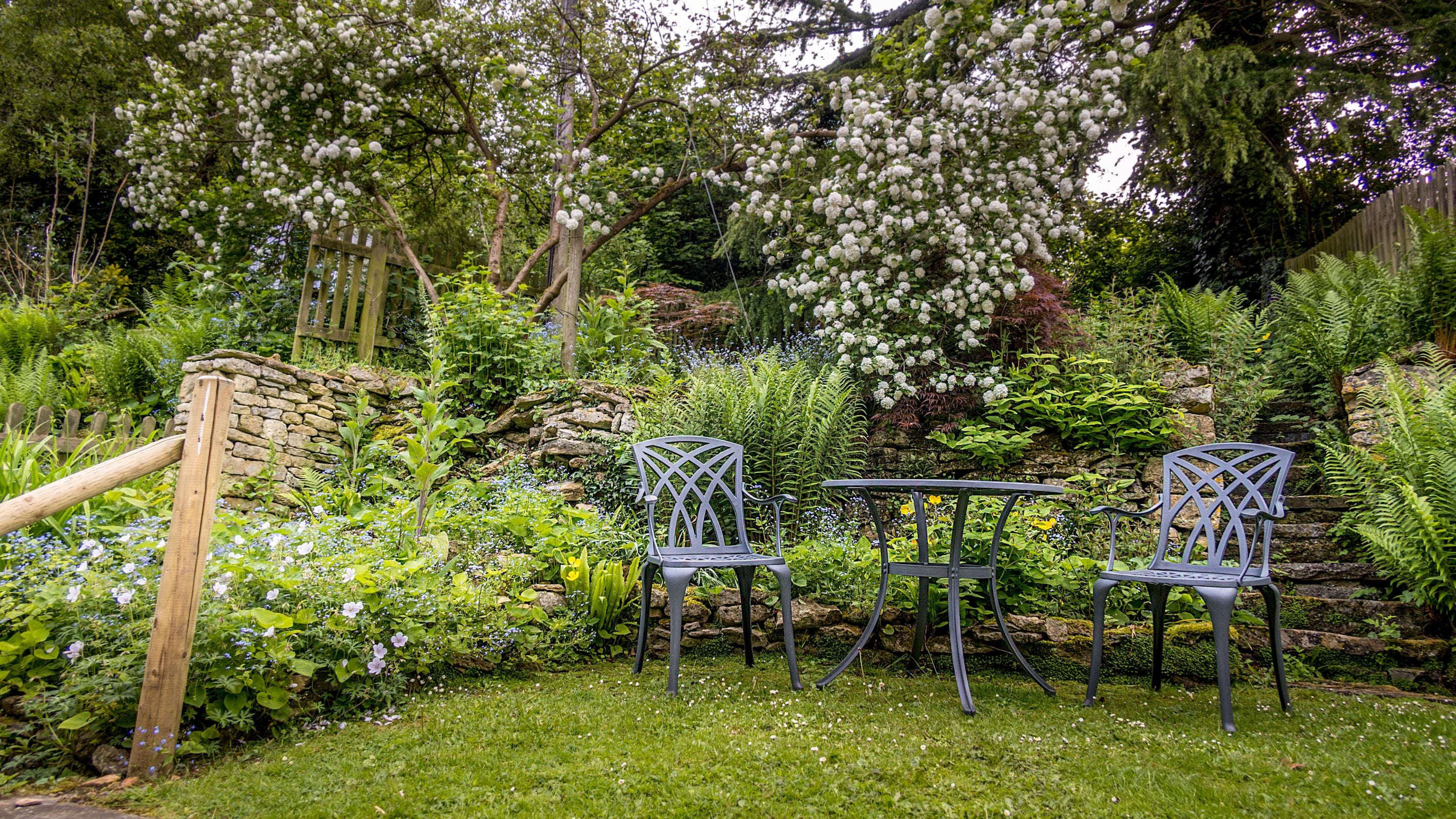 The garden at Spring Cottage in spring, with table and chairs for two, Gloucestershire