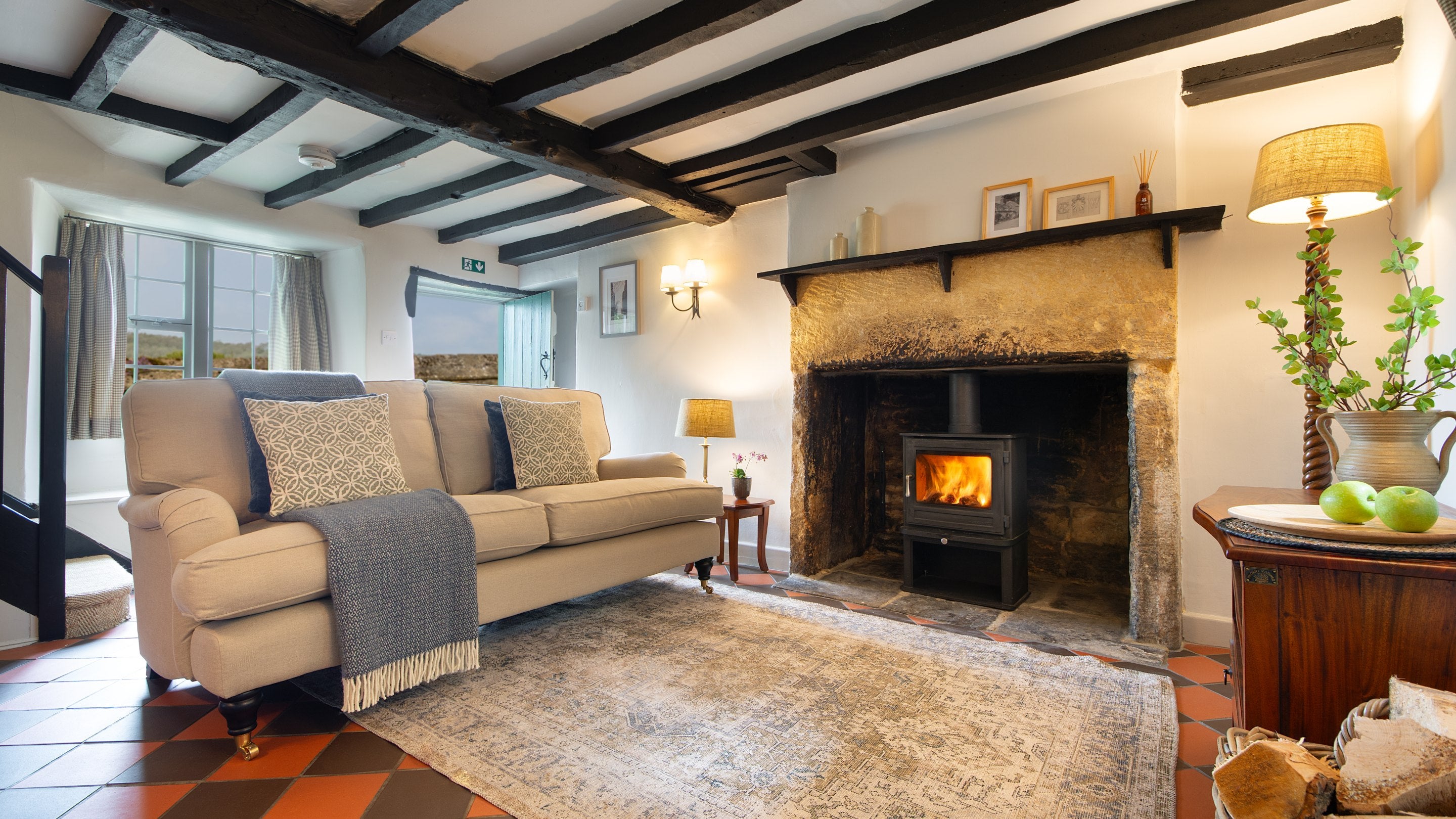 The open-plan sitting and dining room with sofa, woodburner and original beams at Spring Cottage, Gloucestershire