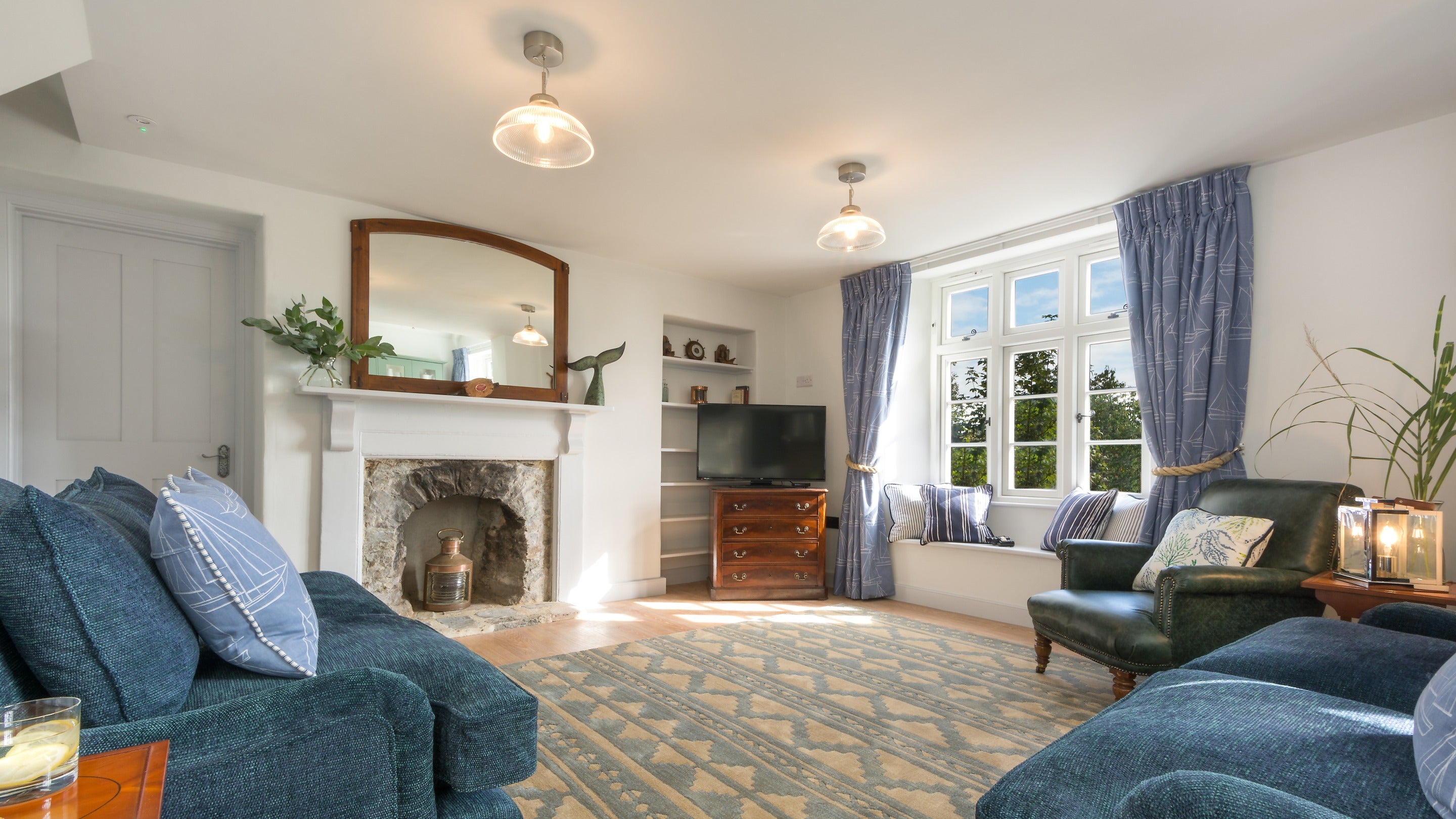 The sitting room area at Compass Cottage, with sofas, armchair, window seat, television and original fireplace, Devon