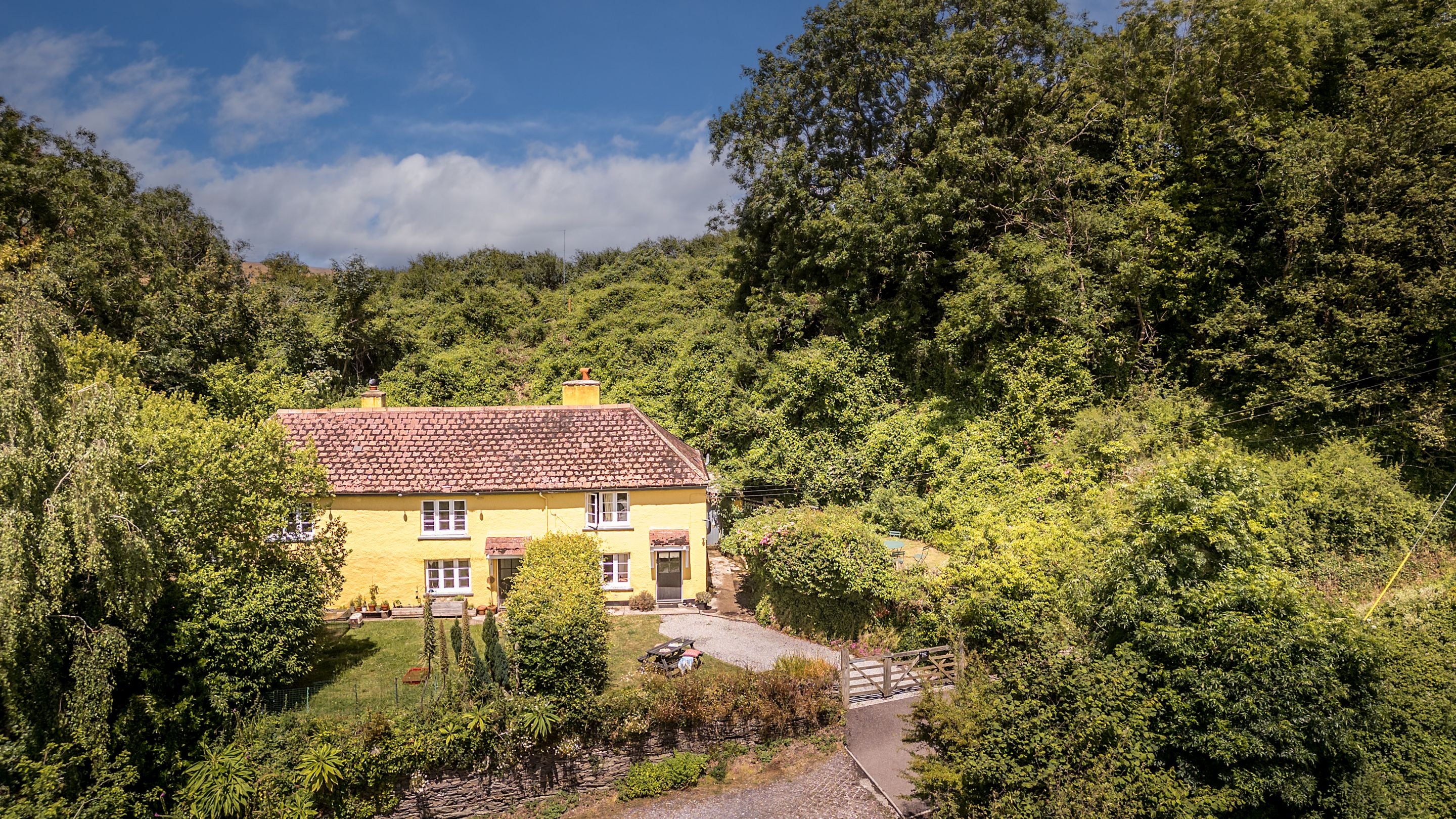 An aerial view of Crockers Cottage, a yellow semi-detached cottage with a red-tiled roof, Devon