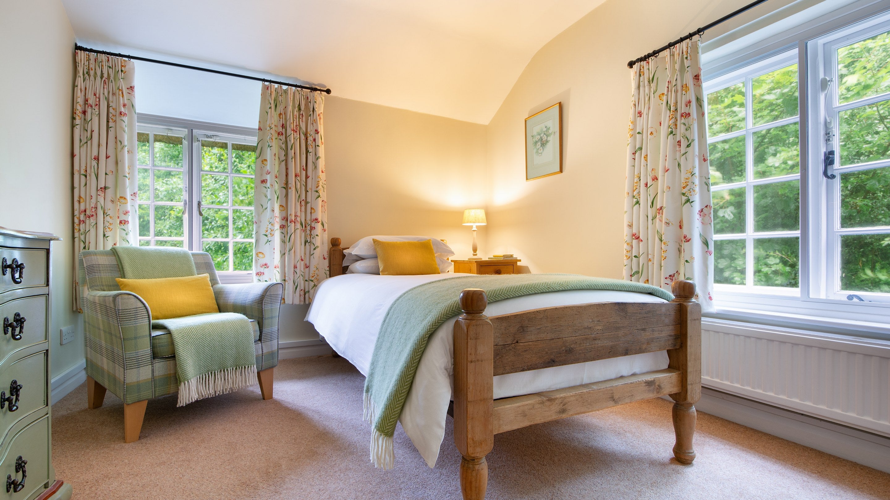 The single bedroom at Ash Cottage, including an armchair and chest of drawers and two windows on different sides of the room, Dorset