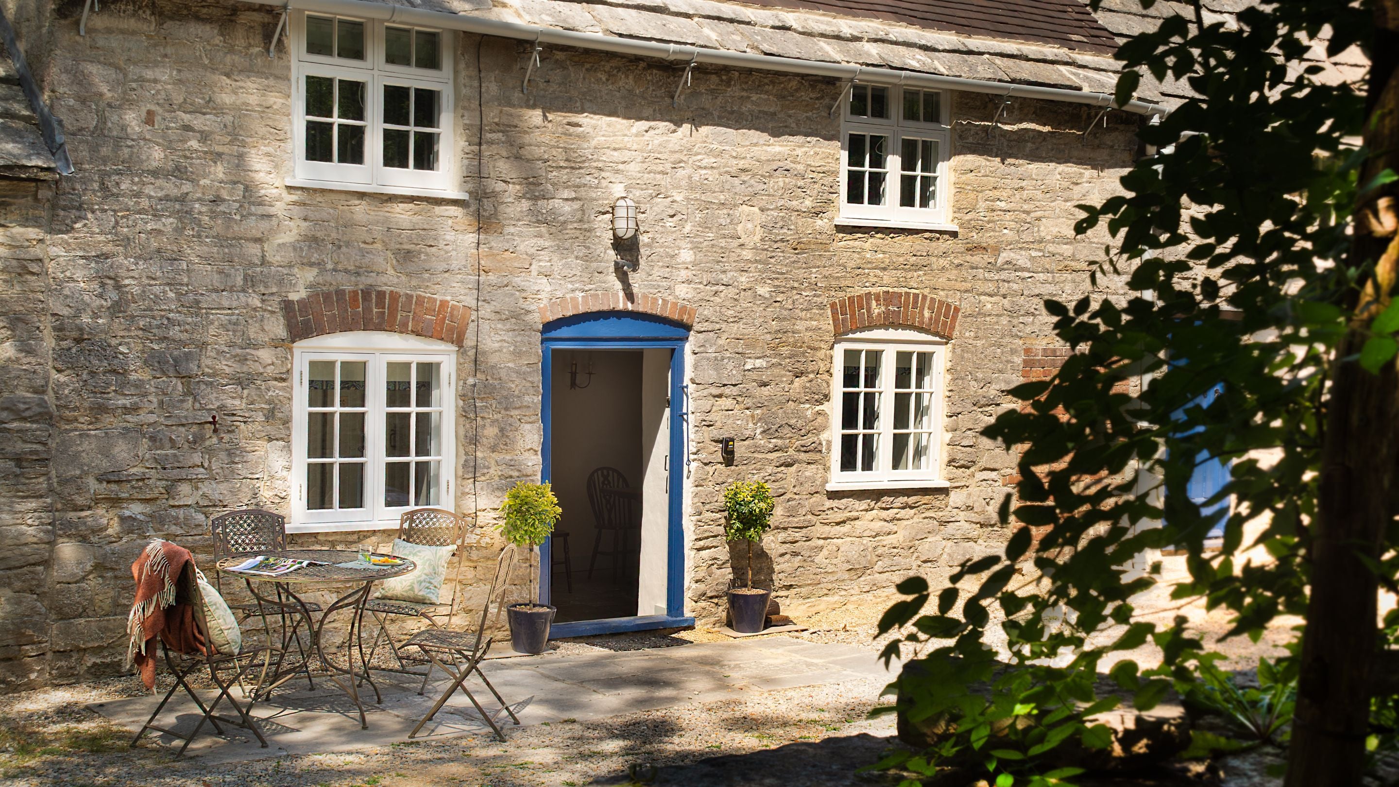 The front of Boar Mill Cottage with outdoor dining furniture on a paved area, Dorset