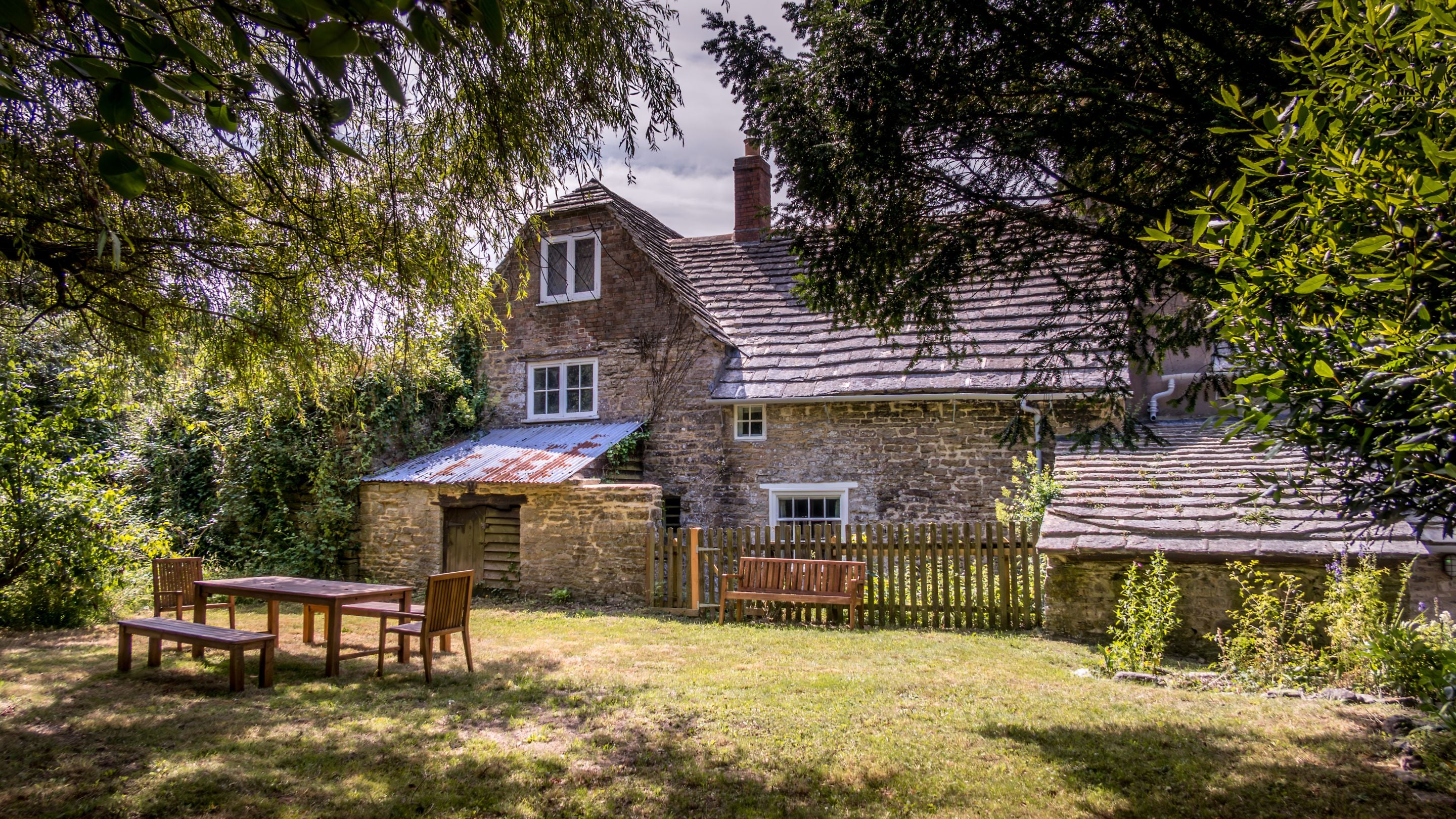 The back garden at Boar Mill Cottage with lawn, trees and outdoor dining furniture, Dorset
