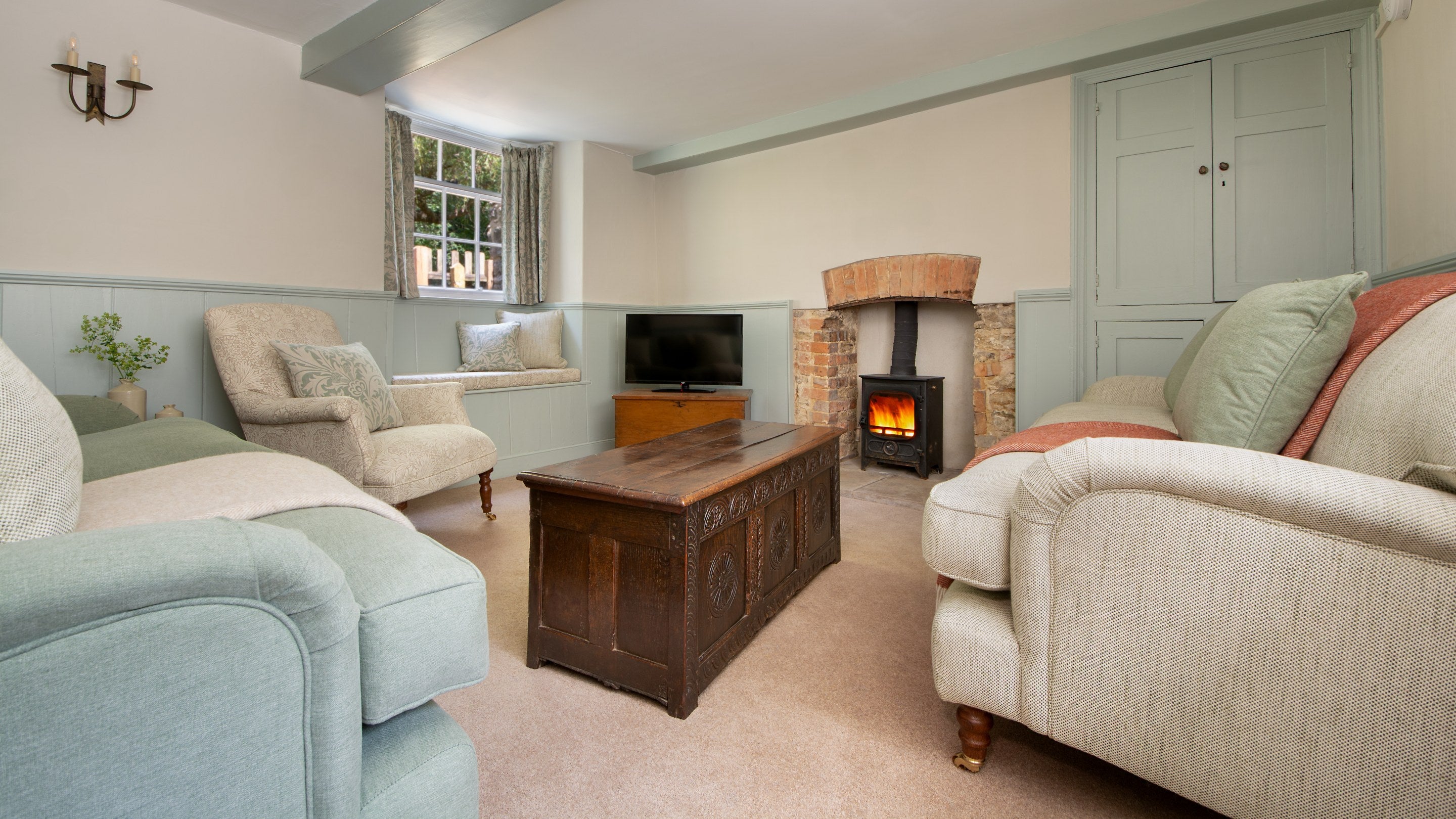 The sitting room at Boar Mill Cottage, with sofas, television, woodburner and window seat, Dorset