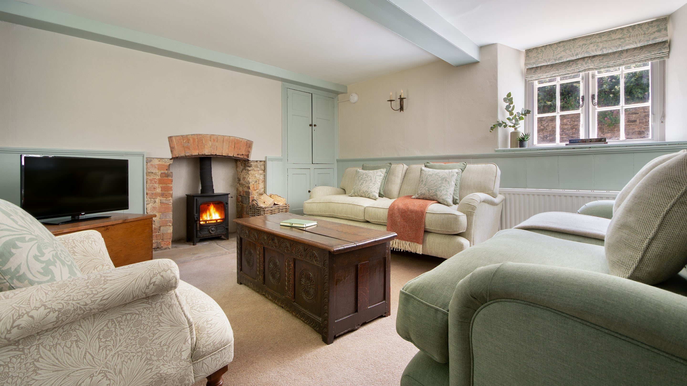 The sitting room at Boar Mill Cottage, with sofas, television, woodburner and window seat, Dorset
