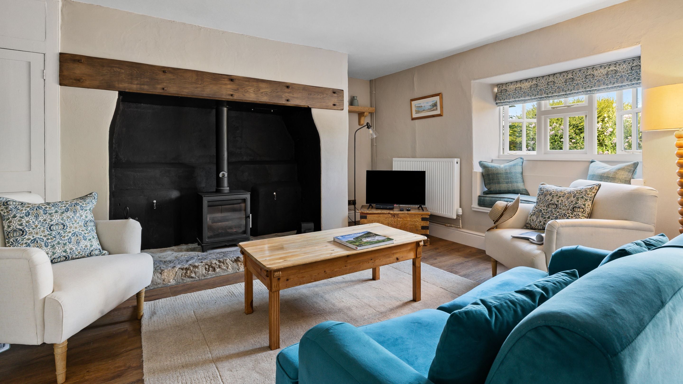 The sitting room at Labour in Vain Cottage with a television, woodburner, a sofa, two armchairs and a windowseat