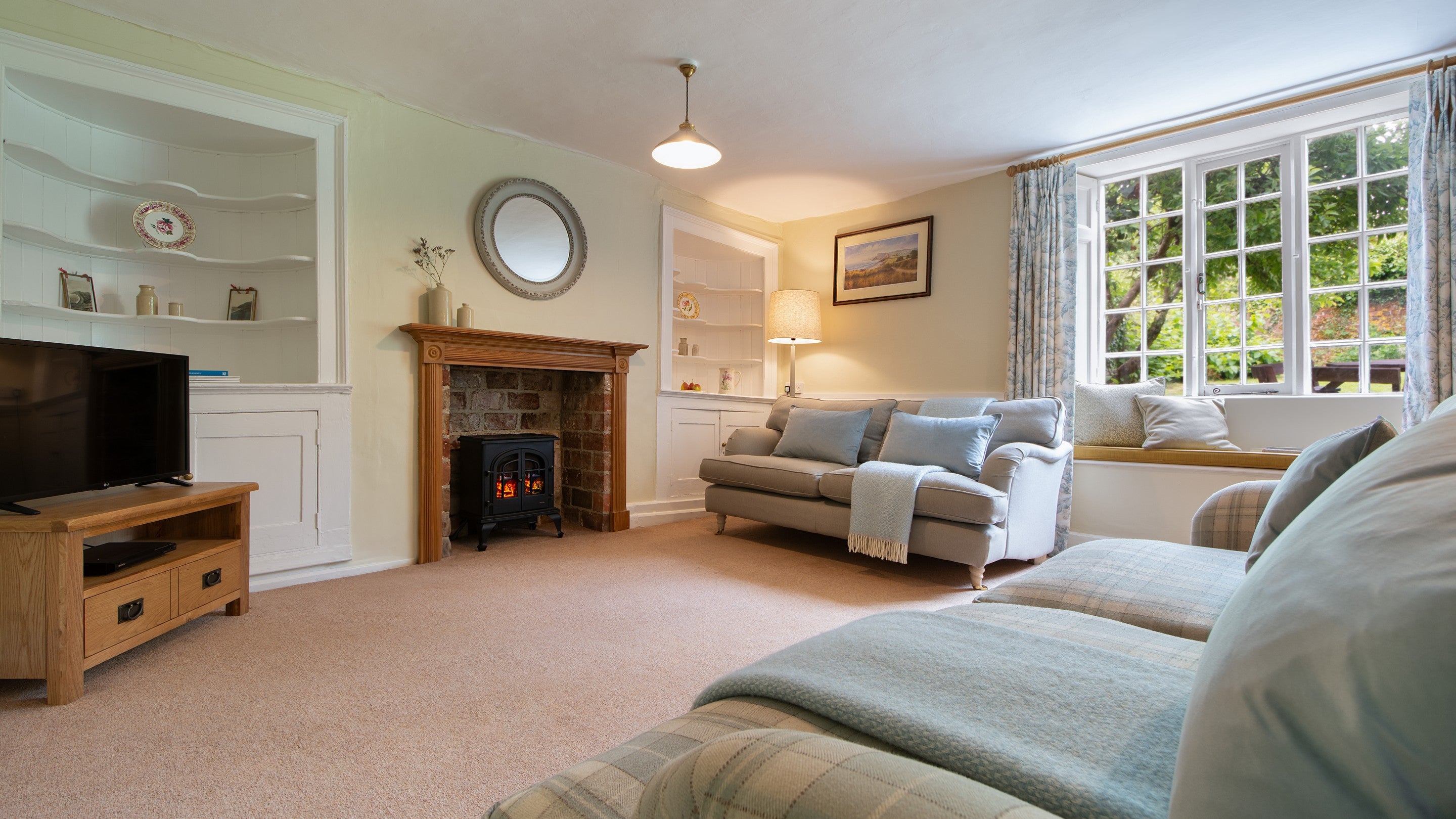 The sitting room at Oak Cottage with sofas, inglenook, television and window seat, Dorset