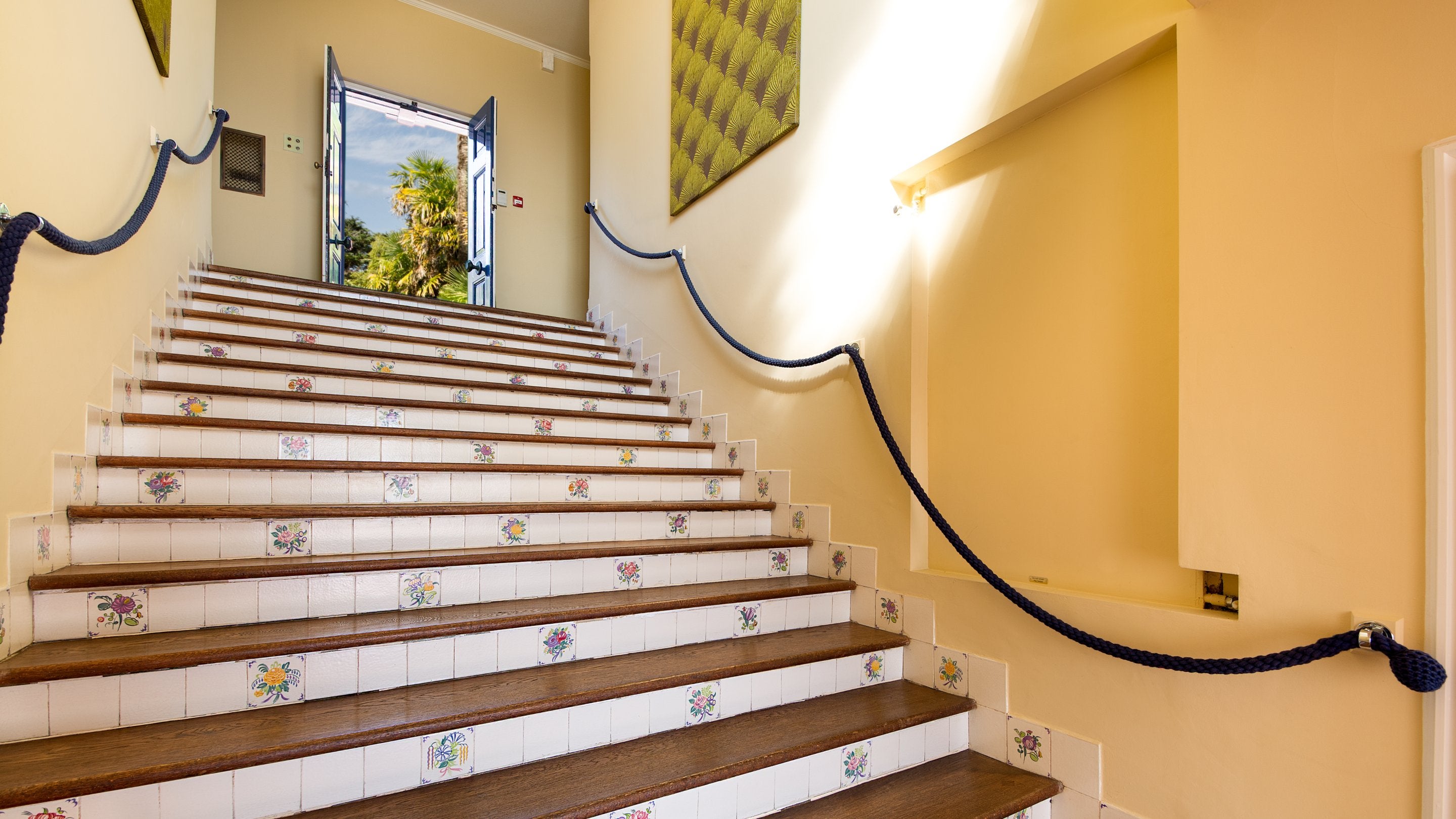 Looking up the main staircase, with rope banisters and period Poole Pottery tiles with floral designs. It leads to the main entrance door on the first floor of Portland House, Dorset