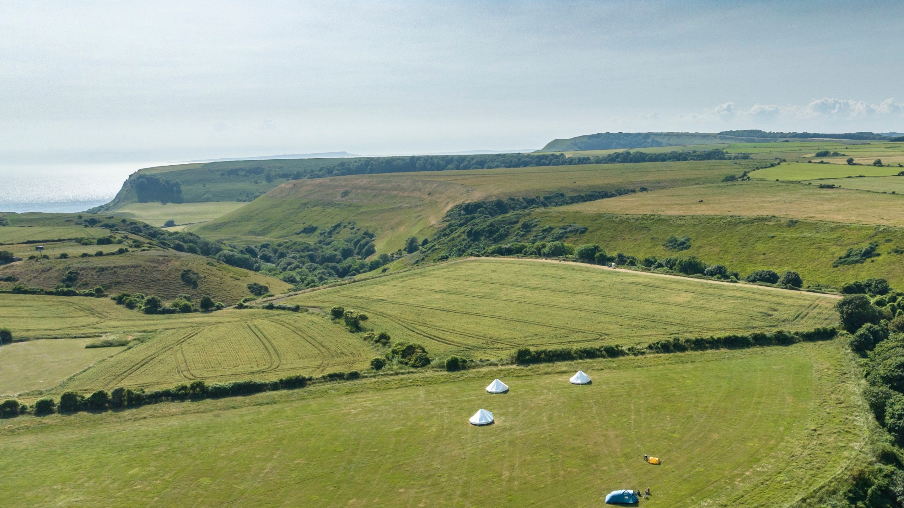 An aerial view of tents and bell tents at Weston Farm Campsite with coastal cliffs in the distance, Dorset