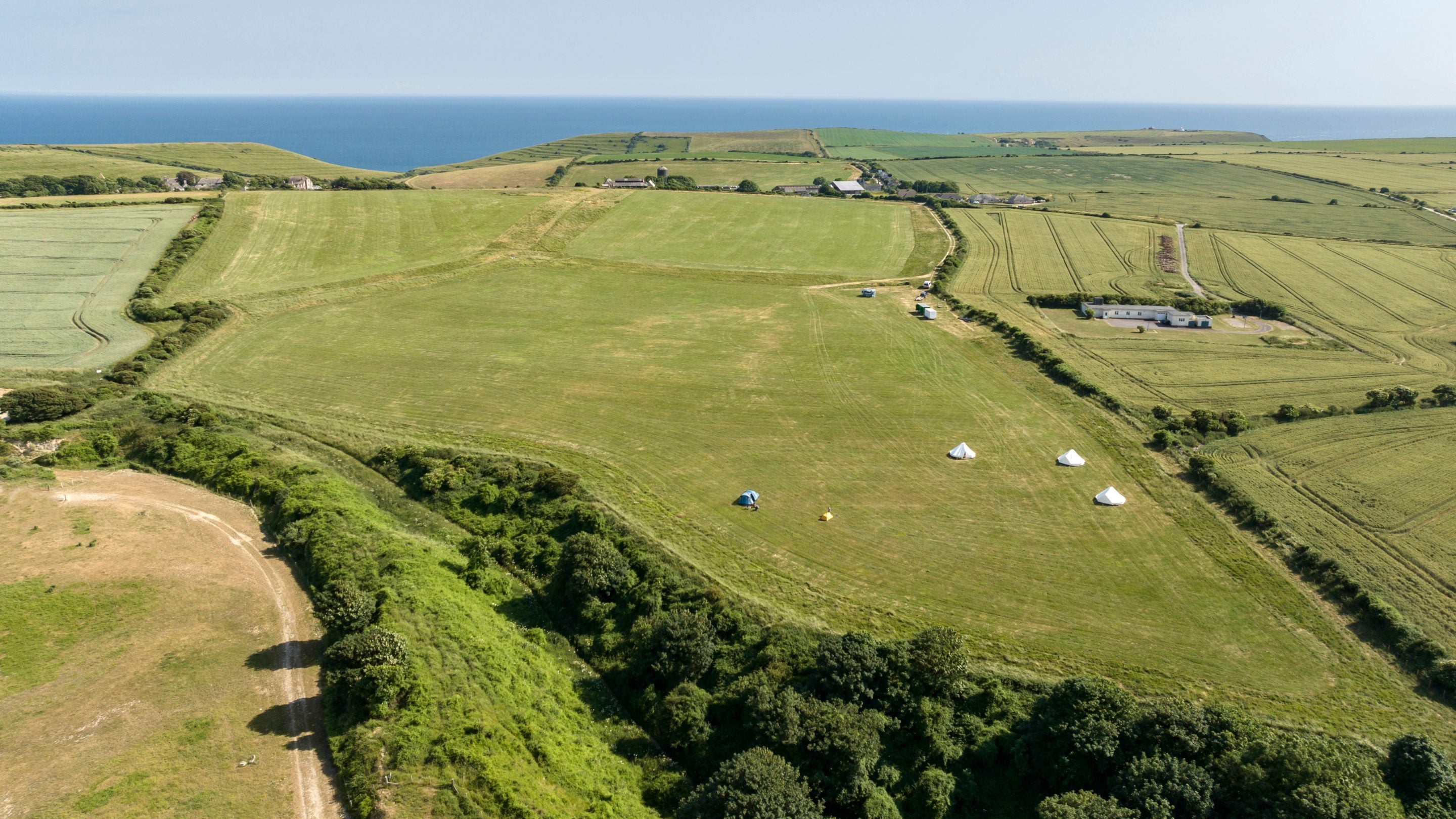 An aerial view of Weston Farm Campsite and the surrounding countryside, with the coast and sea in the distance, Dorset