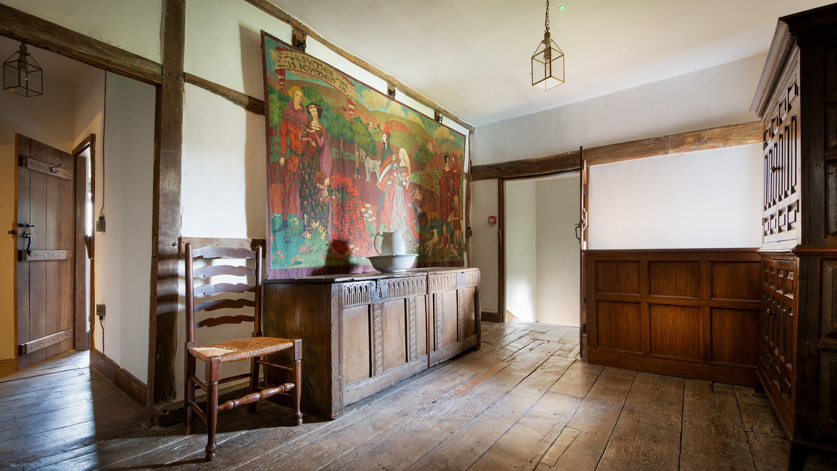 The landing at Cwmmau Farmhouse, with a hand-painted wall hanging, which references a 13th-century poem. It was made in 1928 by Phyllis Jerrold in a medieval style, depicting three medieval couples with dogs, lambs and children in a wooded landscape, Herefordshire