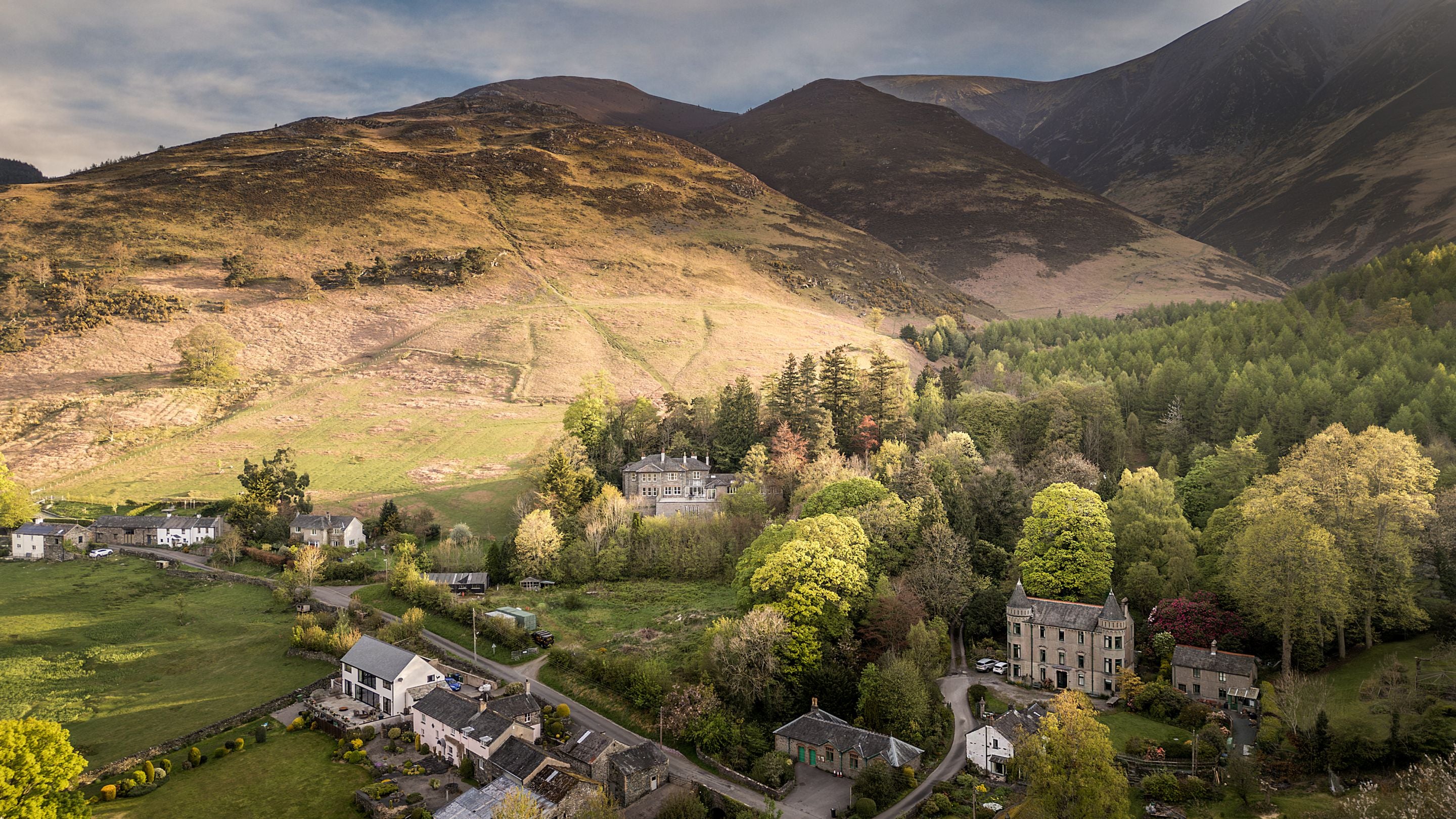 An aerial view of Millbeck village and Millbeck Towers, with Skiddaw to the right, Cumbria