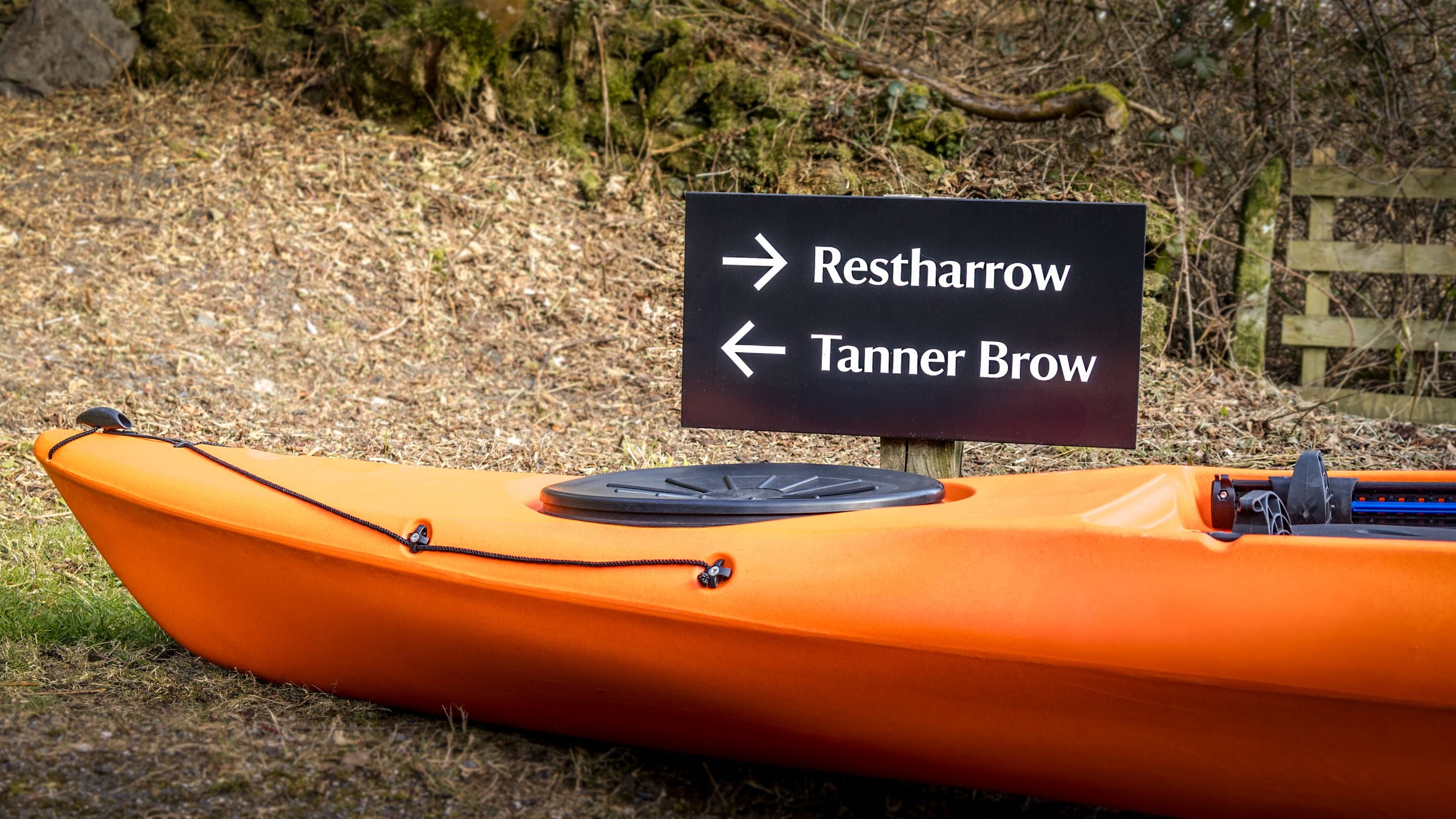 The sign for neighbouring holiday cottages, Tanner Brow and Restharrow, with a kayak resting on the ground next to them, Cumbria