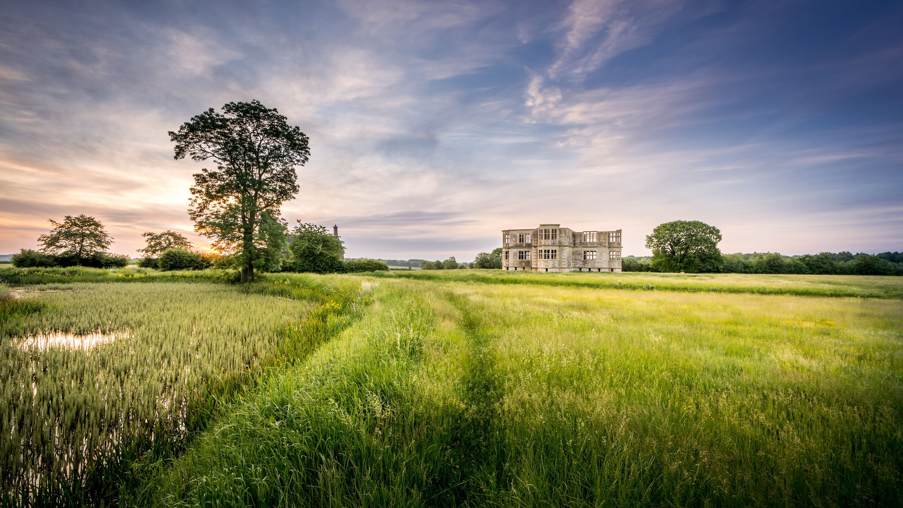 Part of the Lyveden grounds, with a moat, meadow and Lyveden Garden Lodge in the distance, Northamptonshire