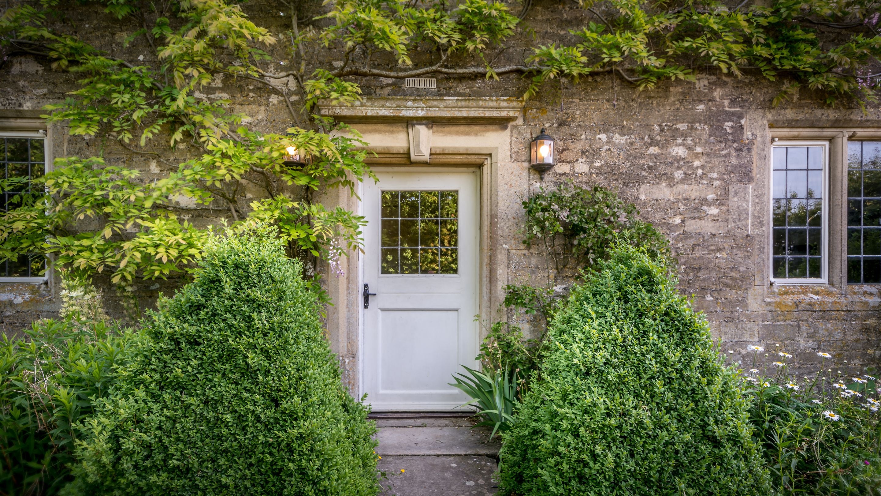Lyveden Cottage's garden door, surrounded by bushes, flower beds and wall climbing plants, Northamptonshire
