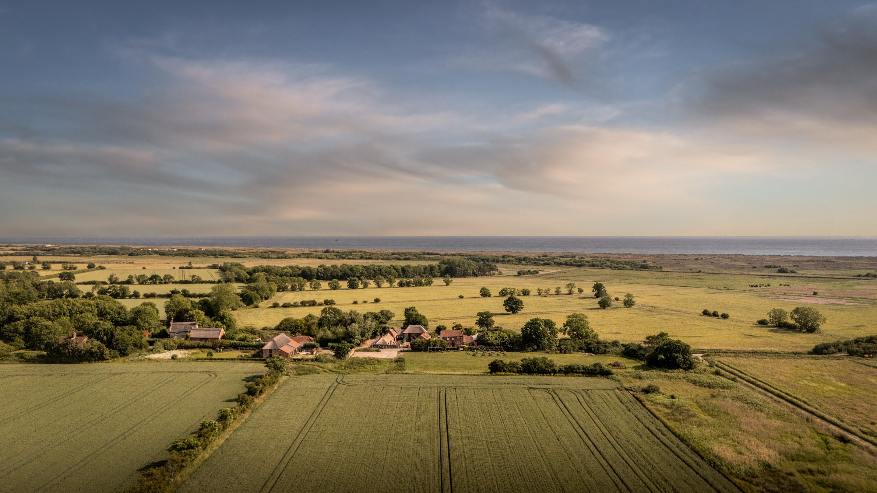 An aerial view of 1, 2 and 3 Horsey Barns with the coast in the distance, Norfolk