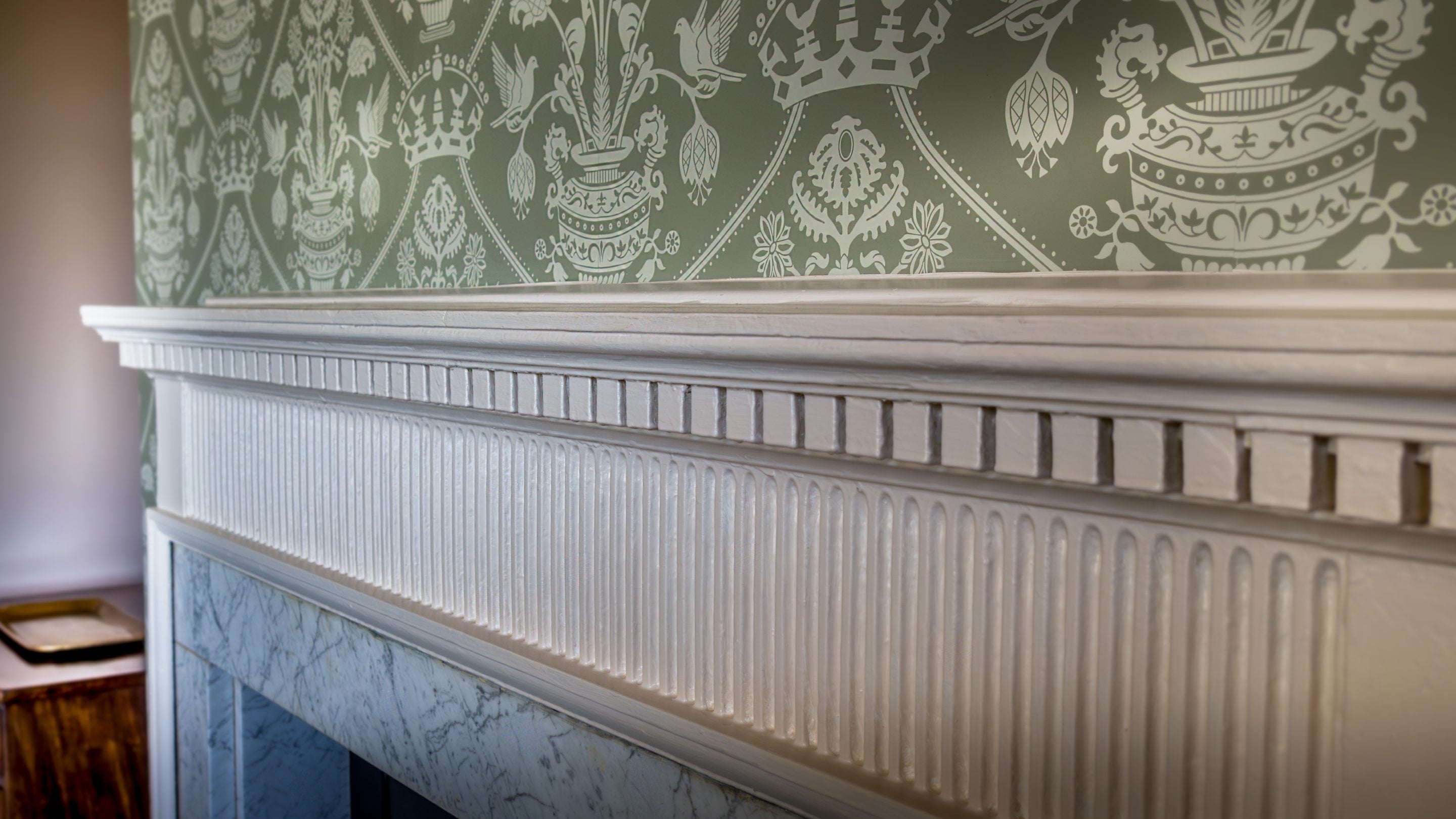 A close-up view of the green patterned wallpaper and ornamental fireplace in the main bedroom on the second floor of Blickling Tower in Norfolk