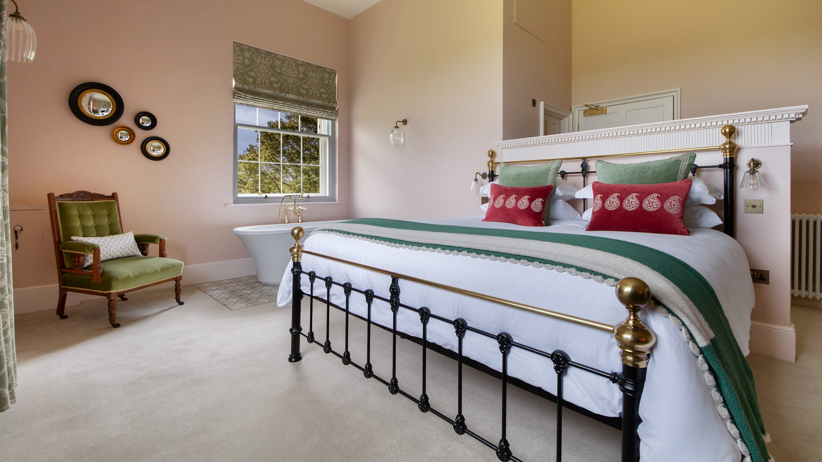 The main bedroom at Blickling Tower with pale pink walls, a super-king bed, green velvet chair and freestanding bath under the window, Norfolk