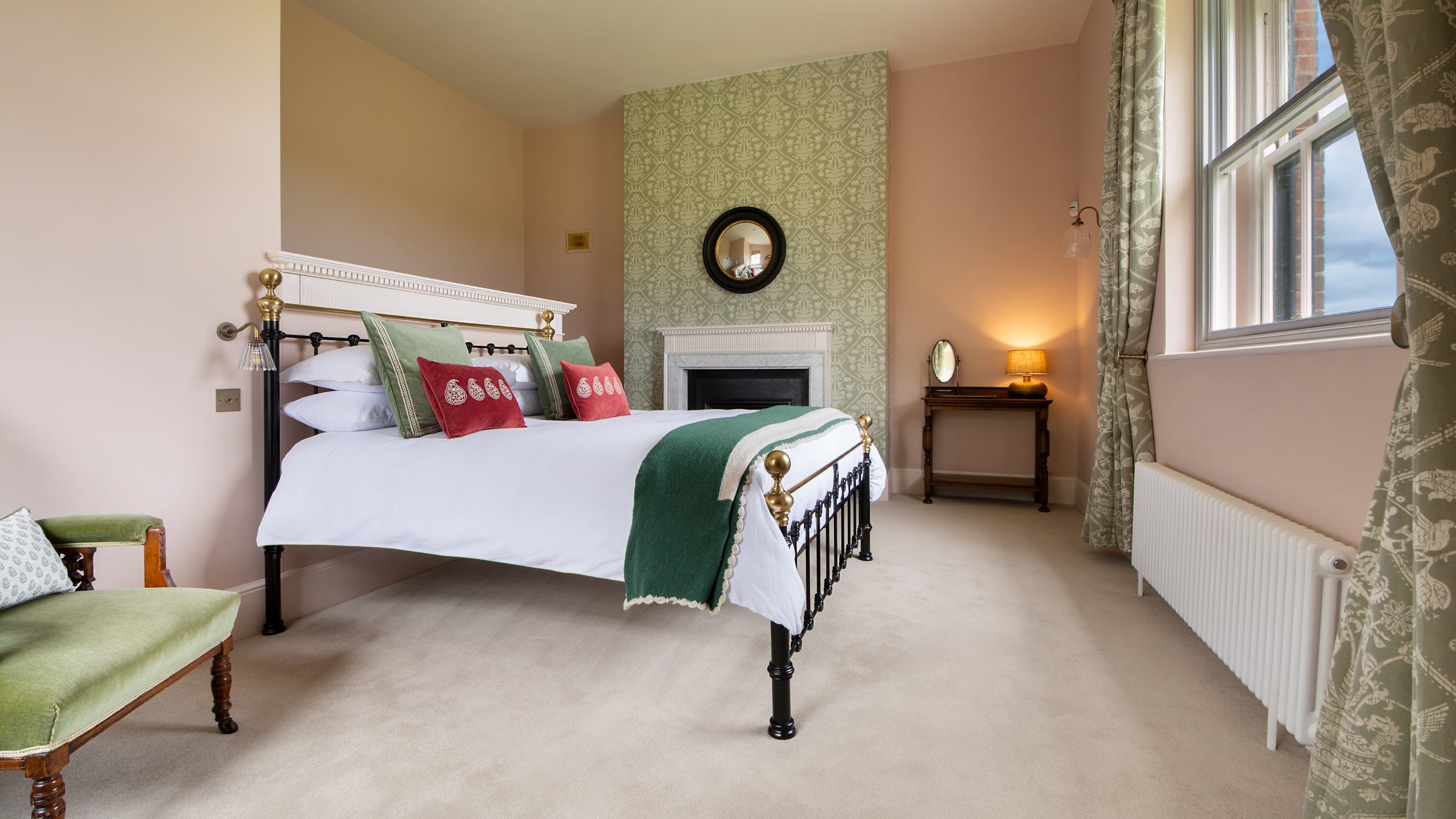 A view of the main bedroom on the second floor at Blickling Tower in Norfolk, showing the ornamental fireplace (which is not in use), the green patterned wallpaper on the chimney breast, the green patterned curtains and a small table with a lamp