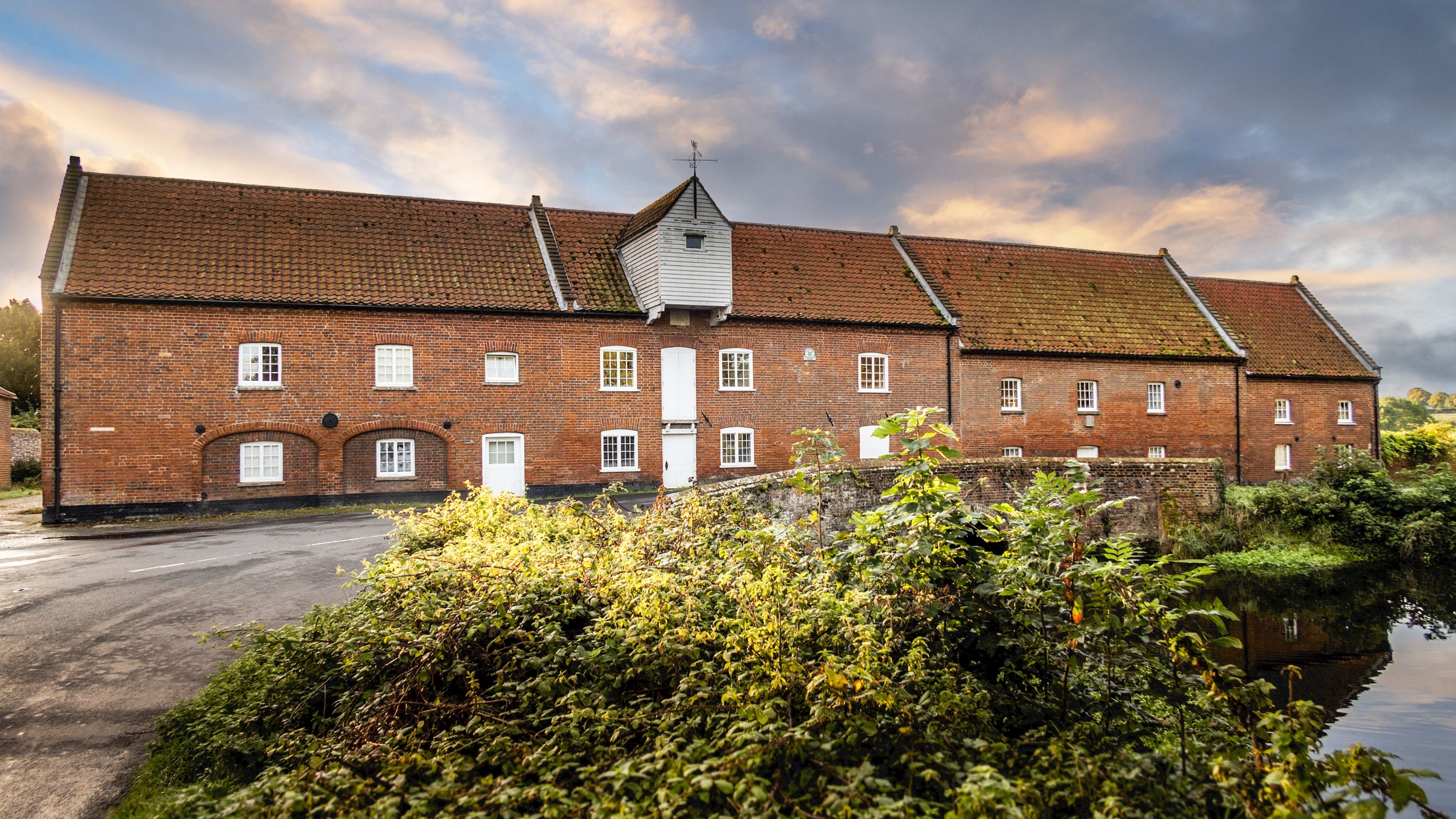 The exterior of the former watermill that houses Millstream and the neighbouring apartments, overlooking the mill pool, Norfolk