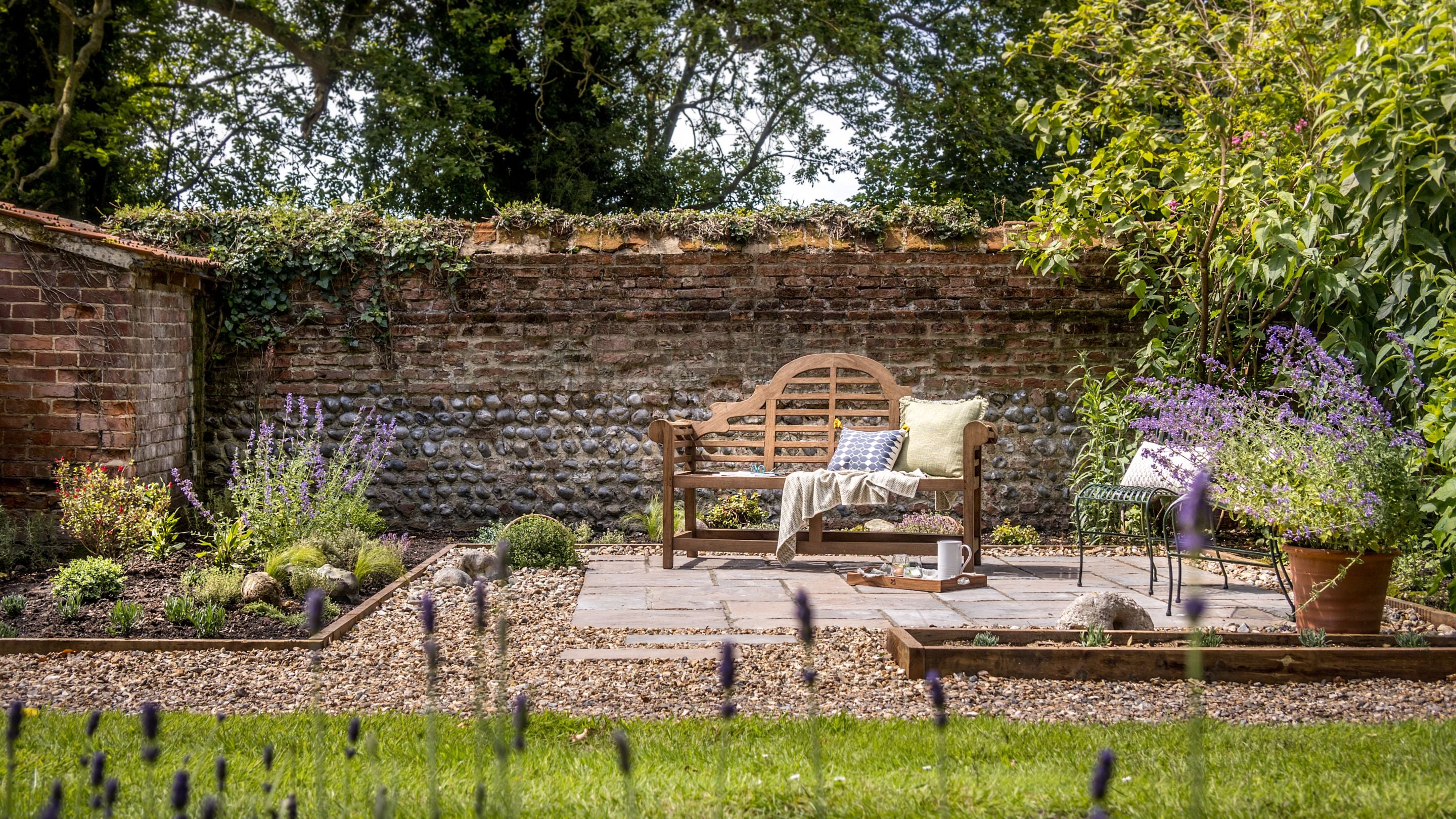 A patio area and bench, surrounded by flower beds and lawn in the garden at Sexton's Lodge, Norfolk