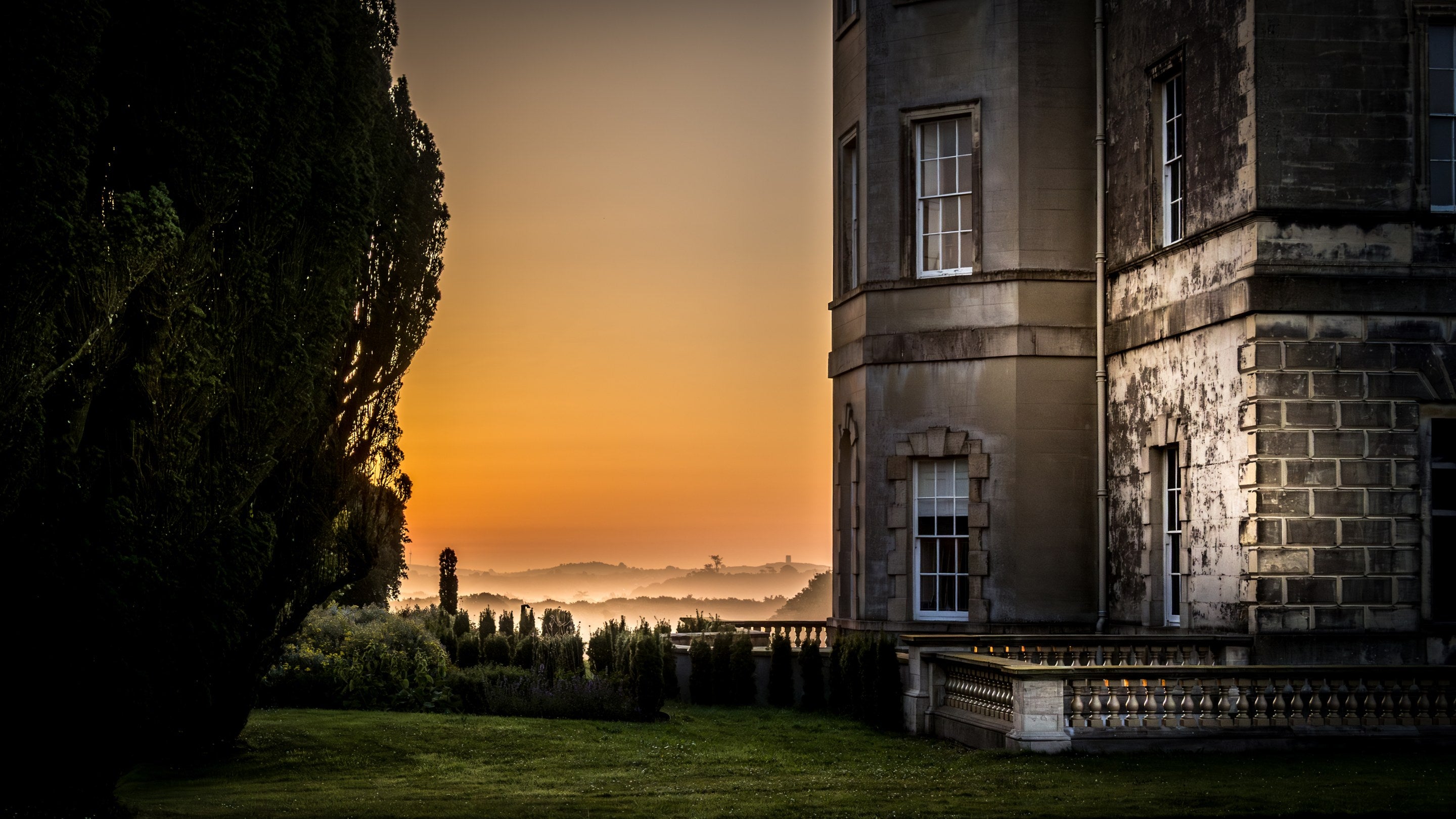 The mansion at Castle Ward and rolling countryside beyond, bathed in orange light at dusk, County Down