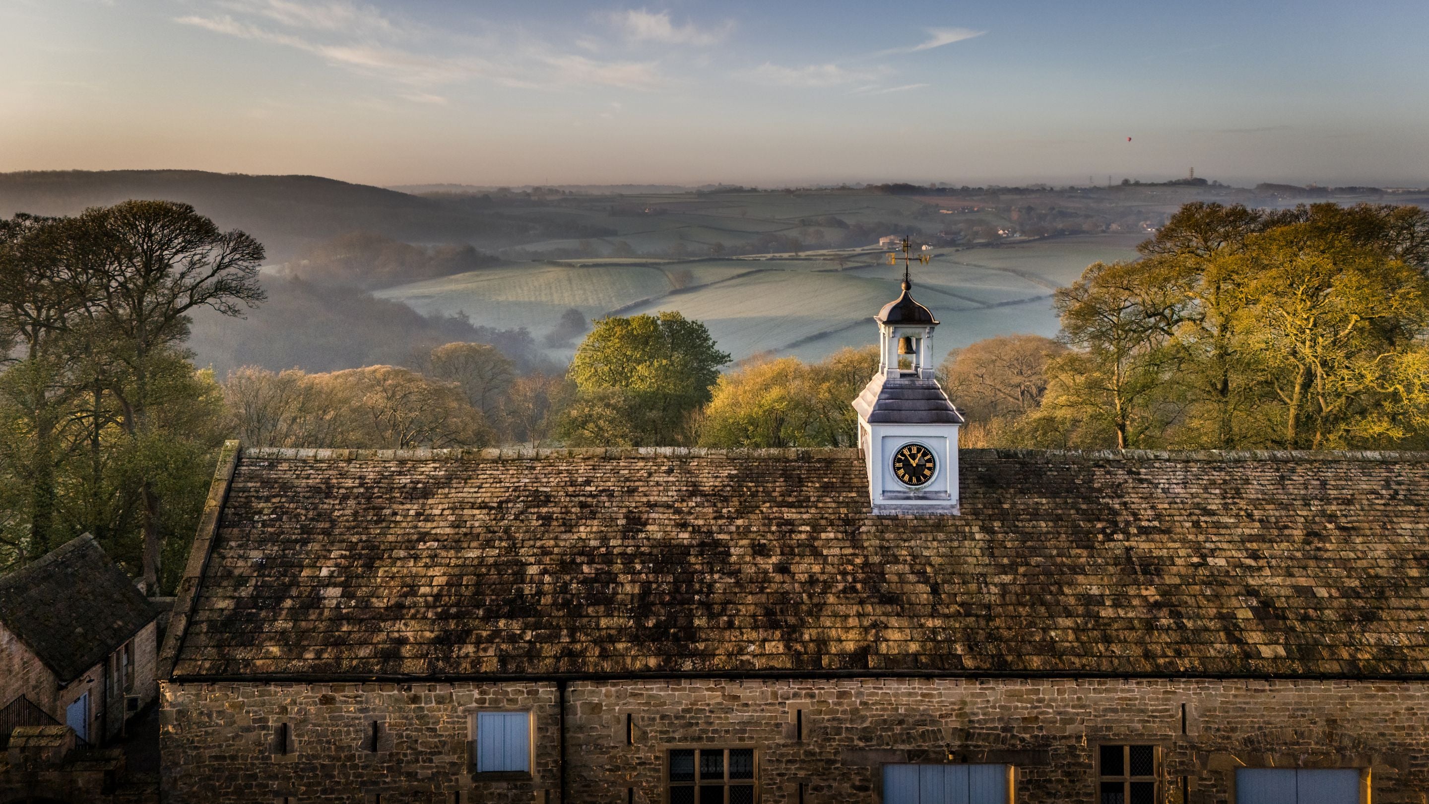 An aerial view of the rooftops and clocktower of Hardwick's Stable Yard and the countryside beyond, Derbyshire